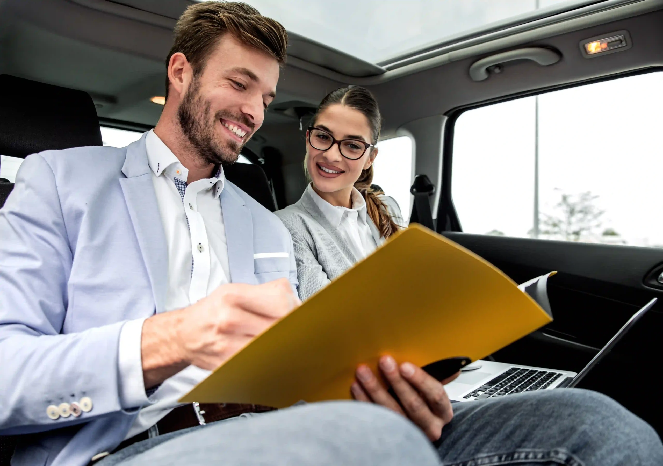 Two business professionals discussing a contract transport auto agreement while traveling in a car.