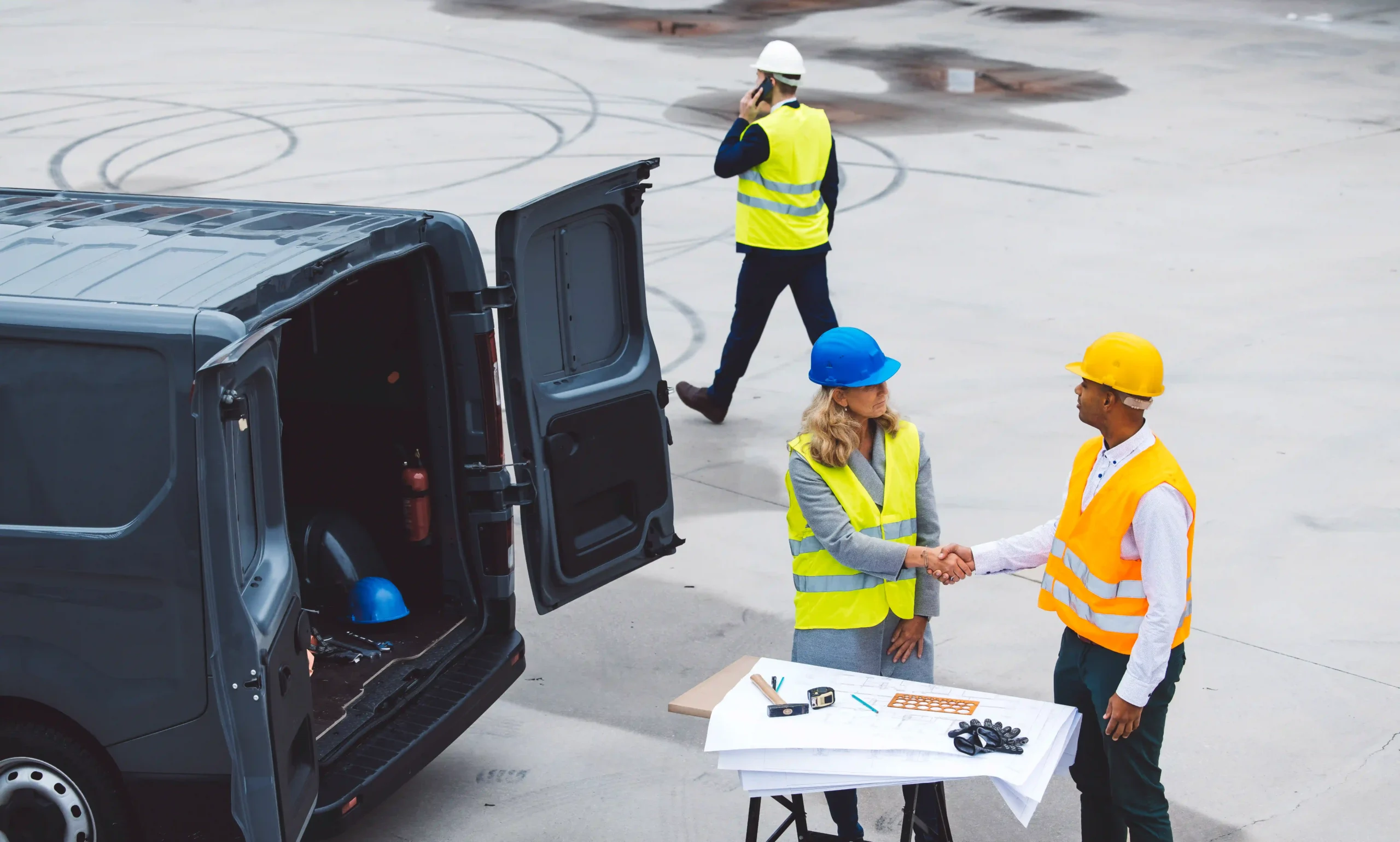 Logistics professionals shaking hands on a contract transport auto deal near a shipping van.