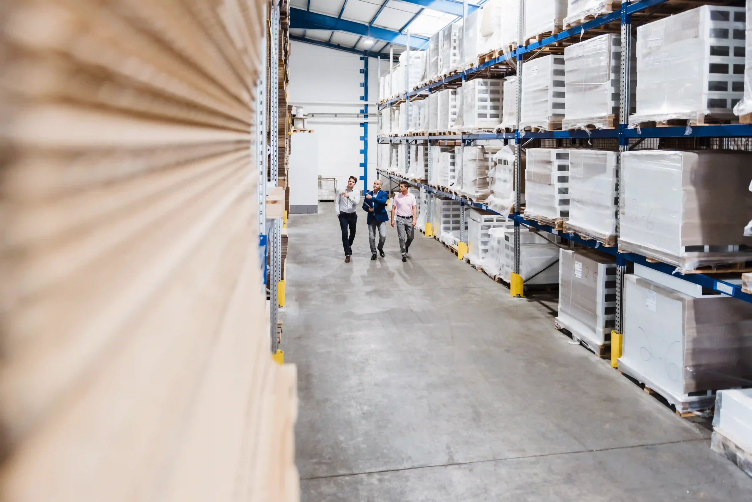 Logistics professionals conducting a facility walkthrough in a cross docking industrial warehouse with high pallet racks.
