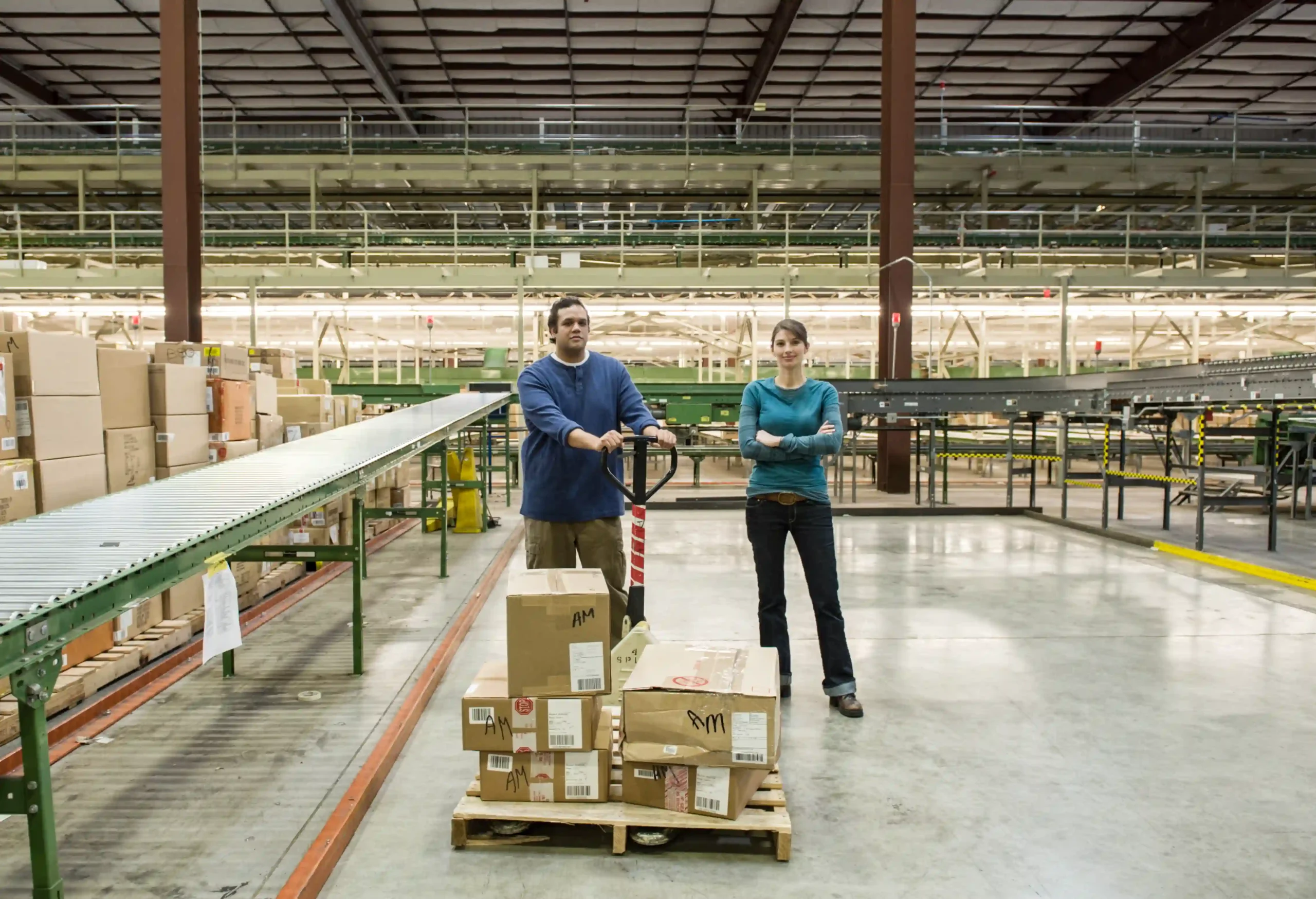 Two warehouse workers standing near conveyor belts in a cross docking industrial distribution center.
