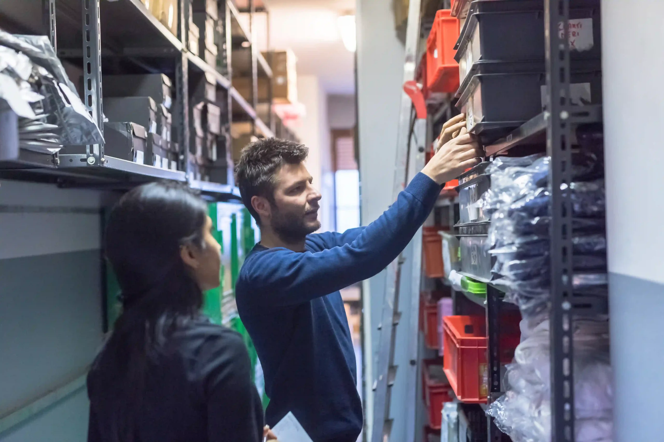 Two warehouse workers reviewing shelves and discussing inventory management questions to improve stock control.