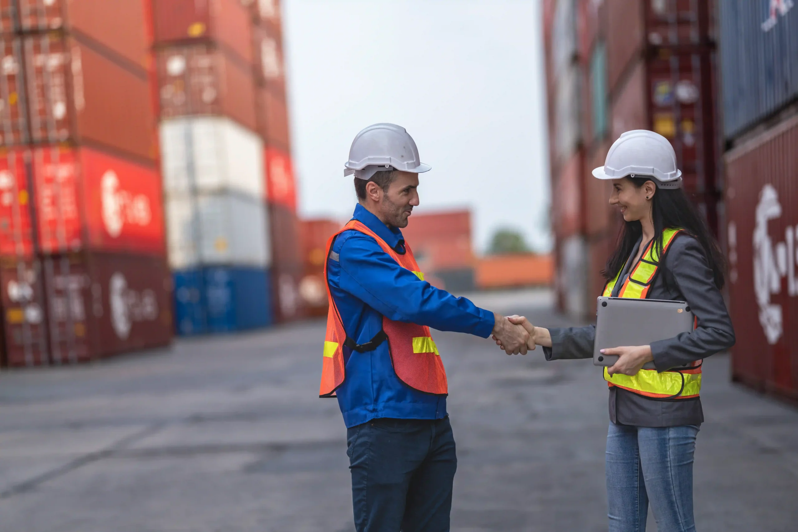 Logistics team members shaking hands at a shipping container yard under a 3PL freight services agreement