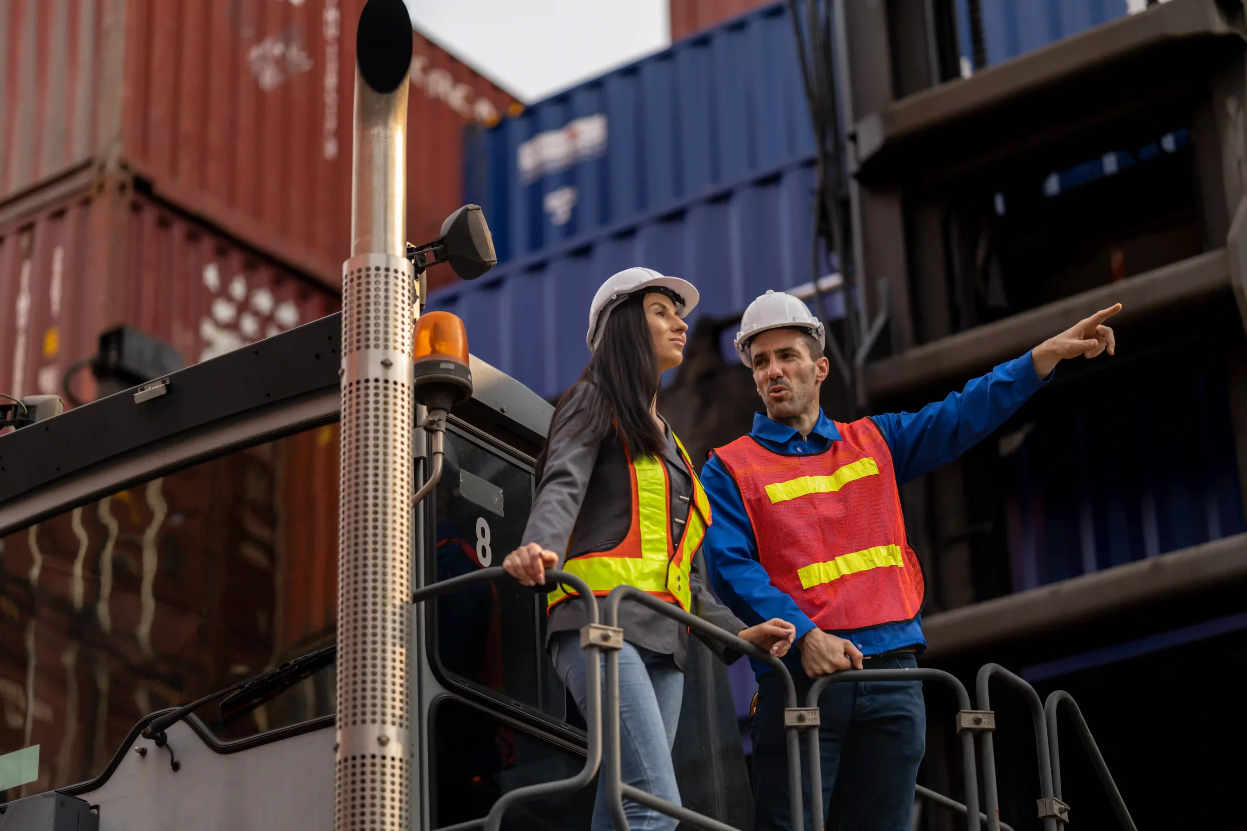 A logistics manager pointing while discussing operations with a colleague atop a container loader, illustrating leadership roles in shipping logistics careers.