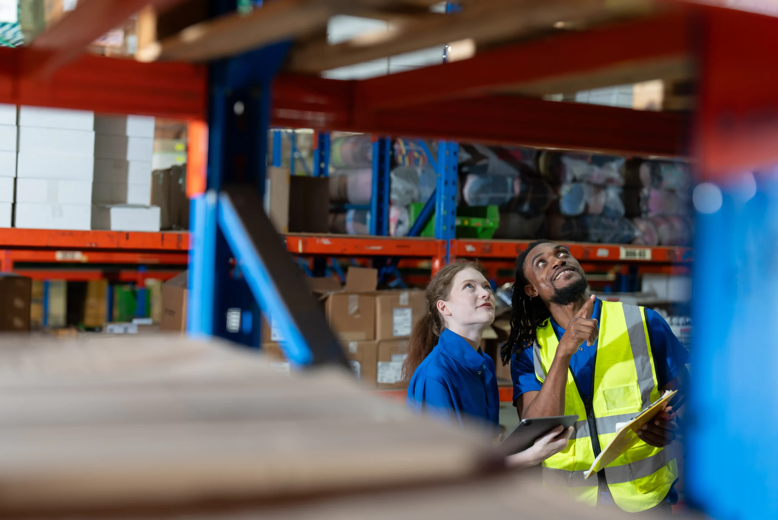 Warehouse workers examining stock shelves with a tablet and clipboard, ensuring accurate inventory management.