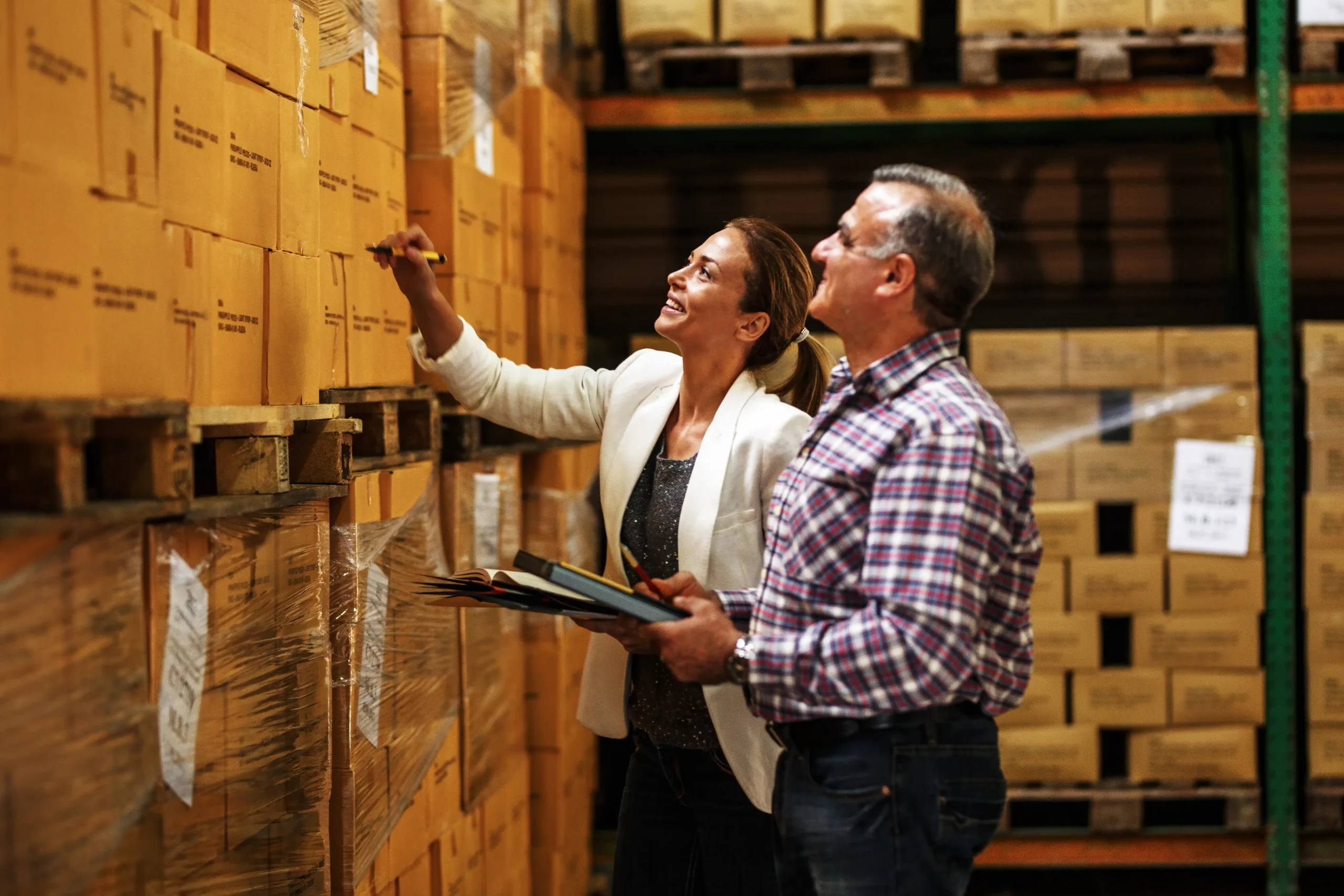 Two logistics experts checking and labeling boxes in a storage warehouse with organized shelves.