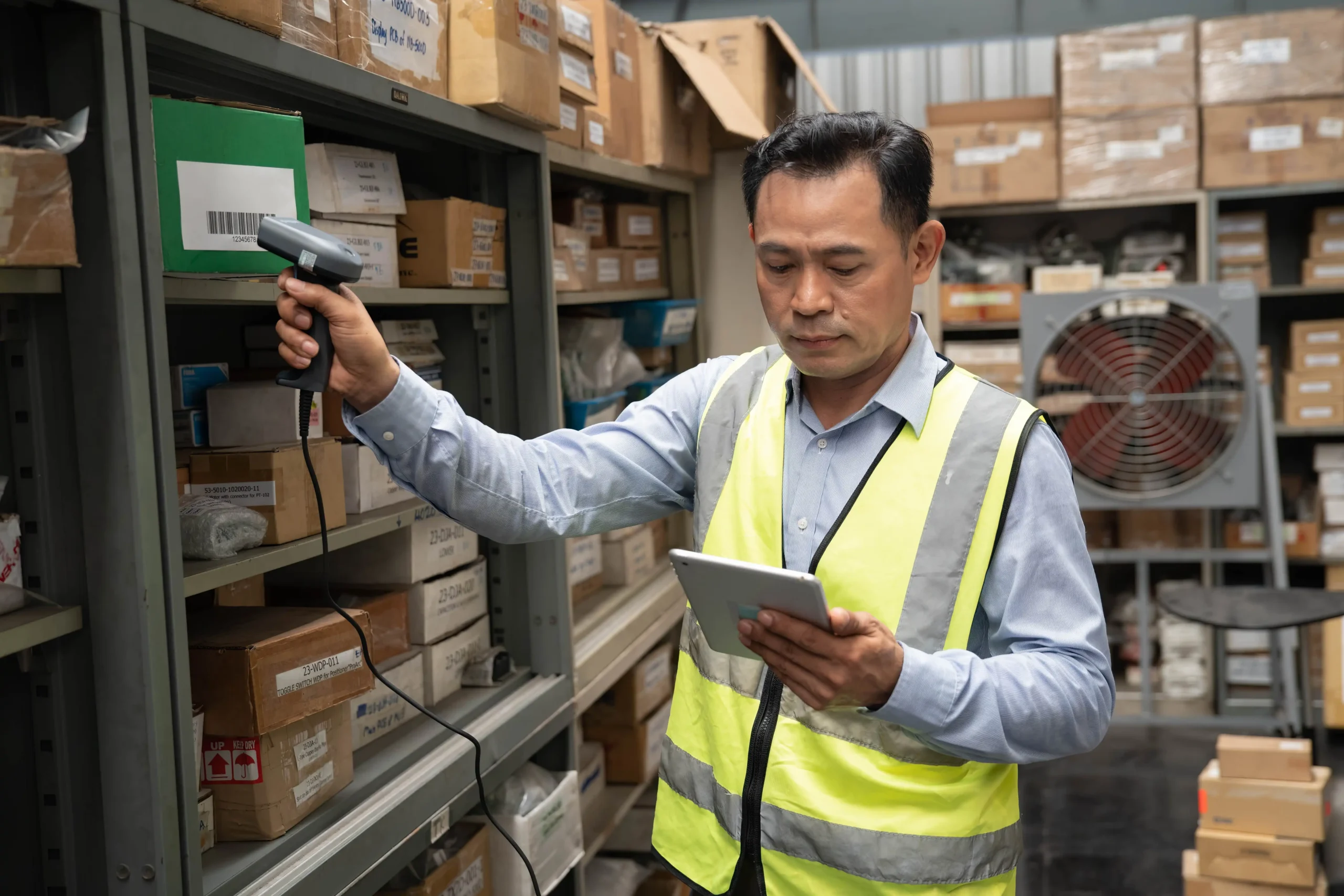 Female warehouse employee using a computer for inventory management while a colleague handles storage bins.