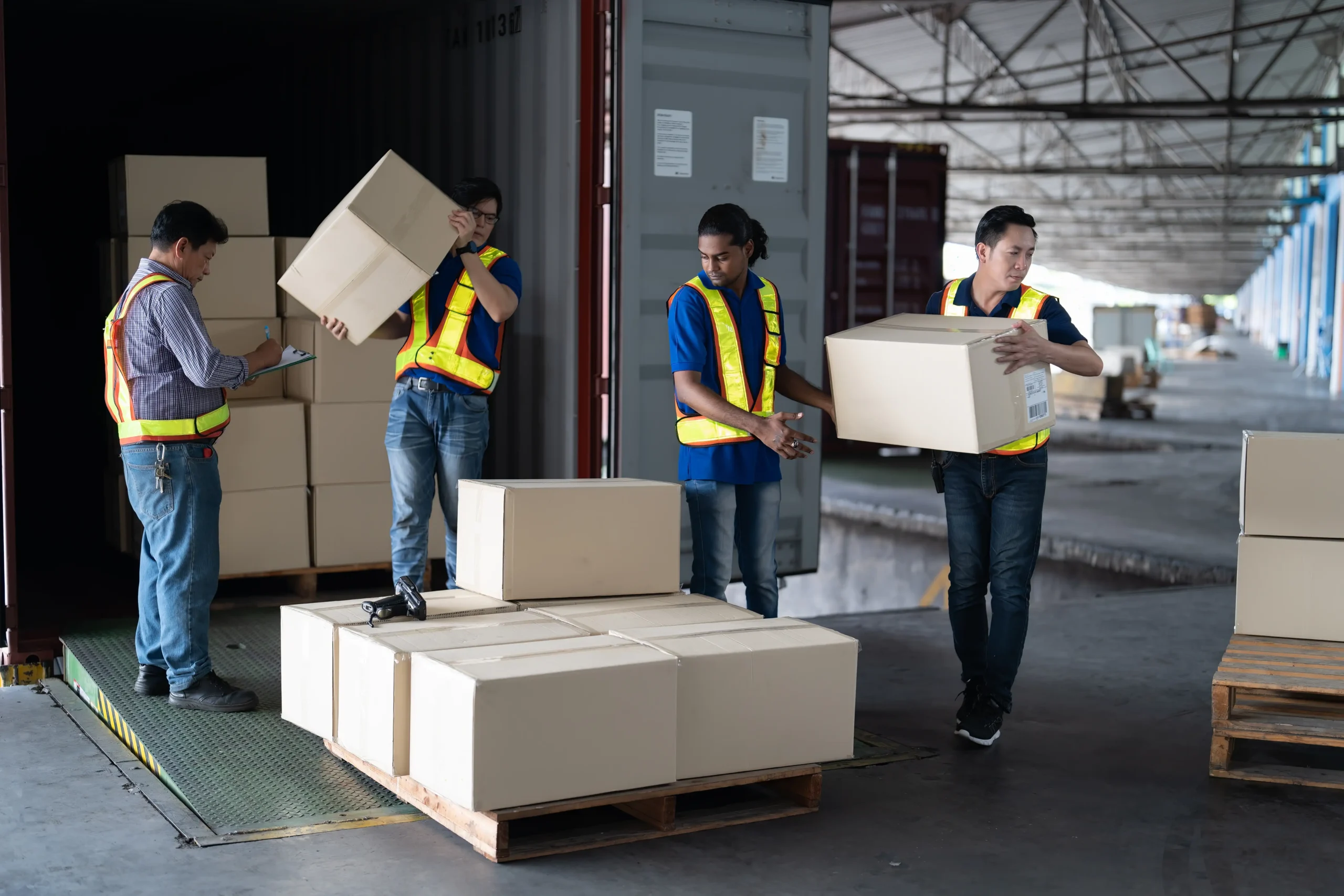 Logistics team unloading boxes from a container in a warehouse, emphasizing teamwork in supply chain operations.