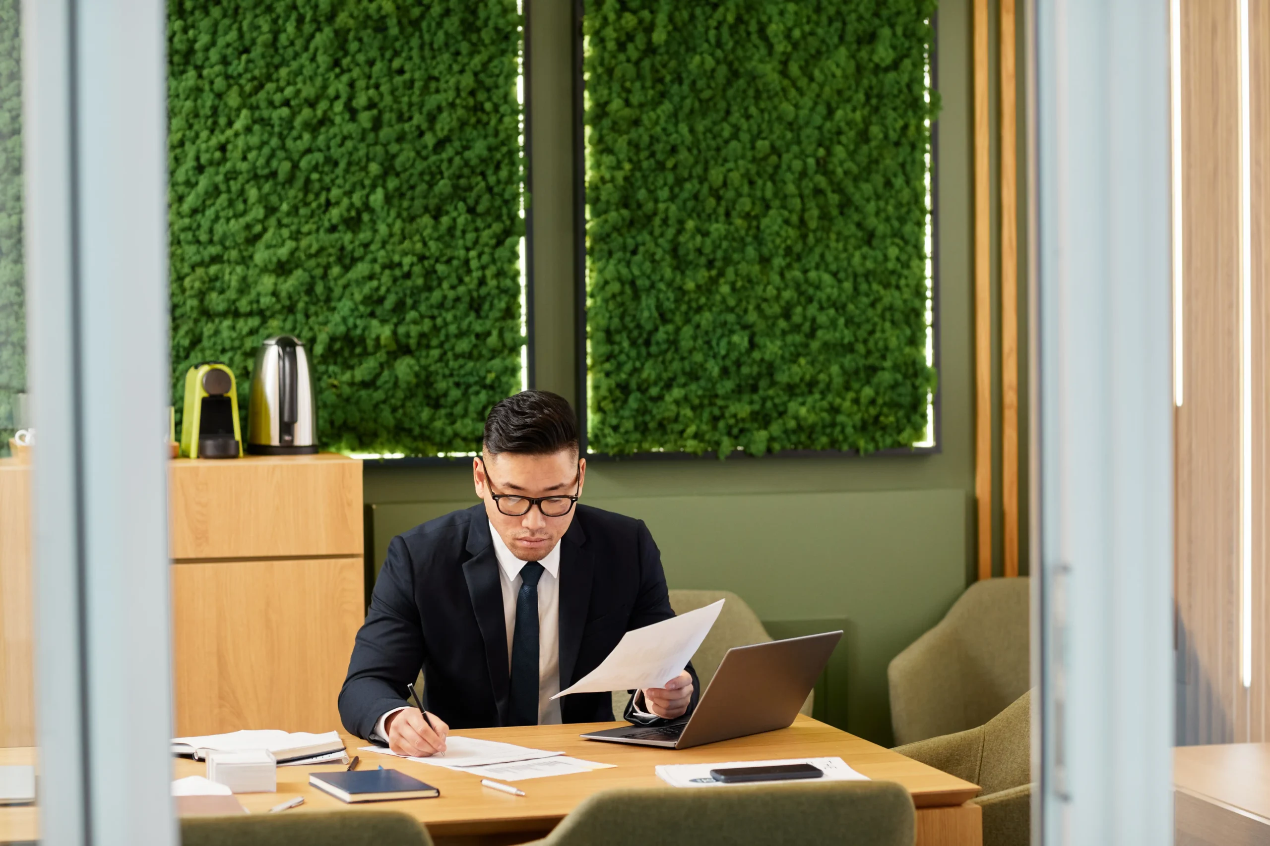 Asian business owner working in a sustainable office with green wall decor and eco-friendly furnishings.