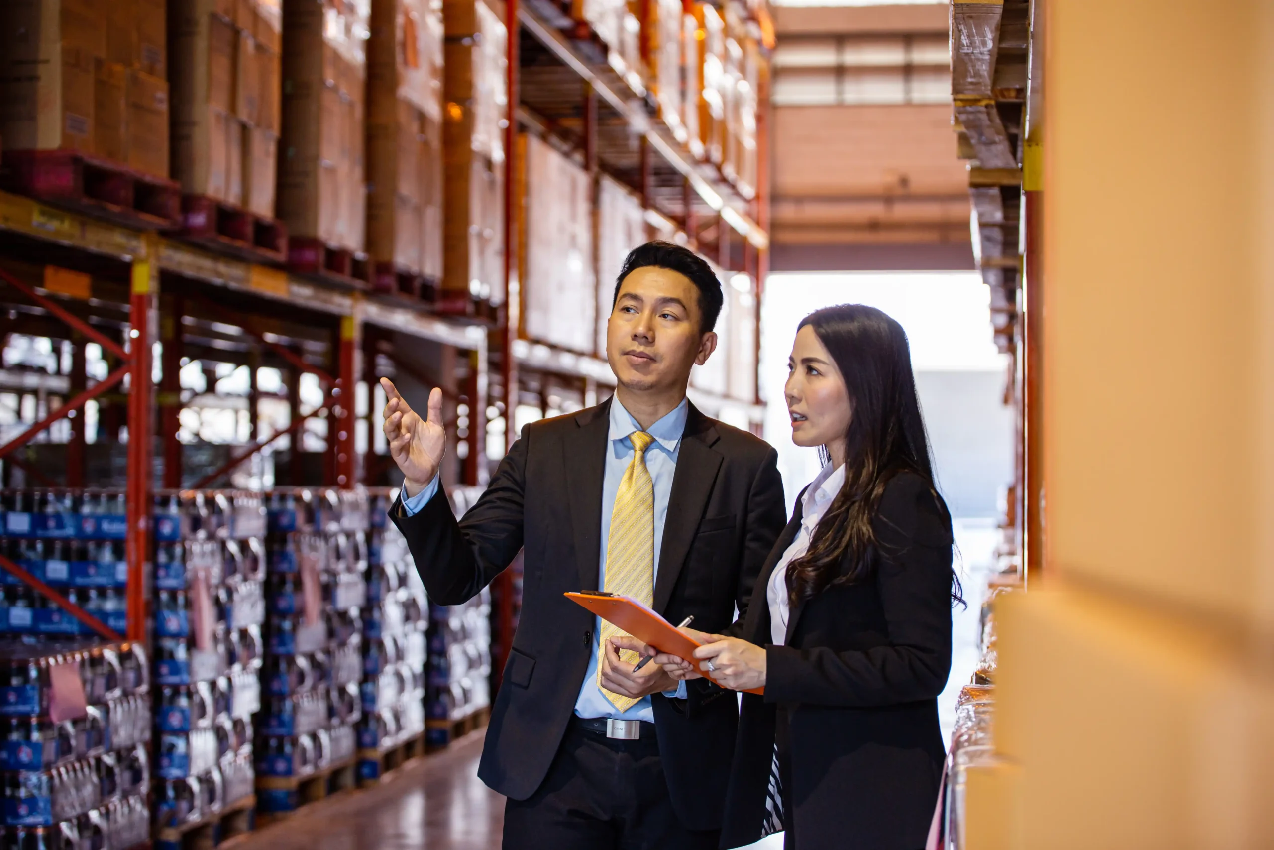 Two business professionals discussing product inventory and regulatory requirements in a modern warehouse.