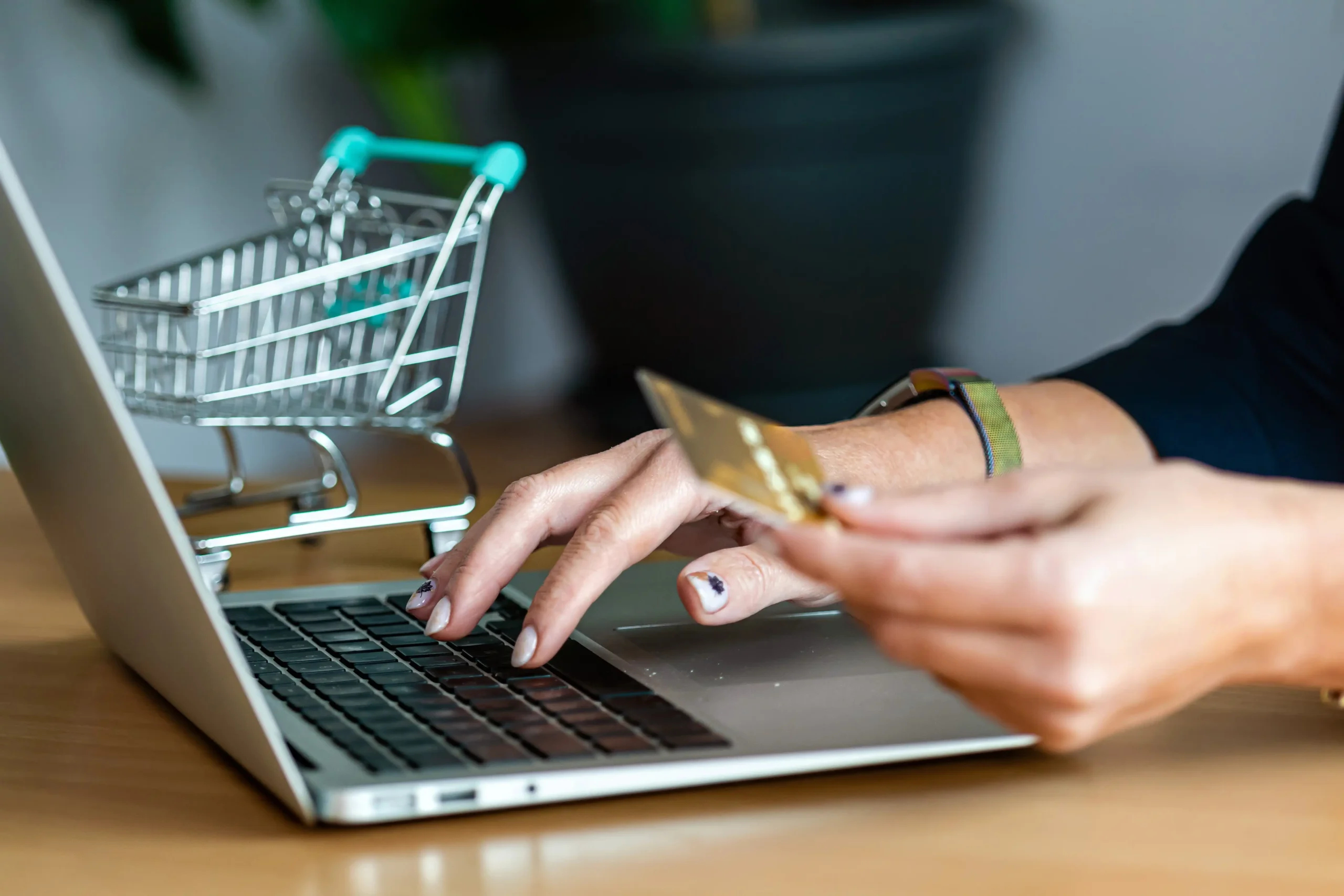 Close-up of a hand entering credit card details for online shopping, with a miniature shopping cart in the background.