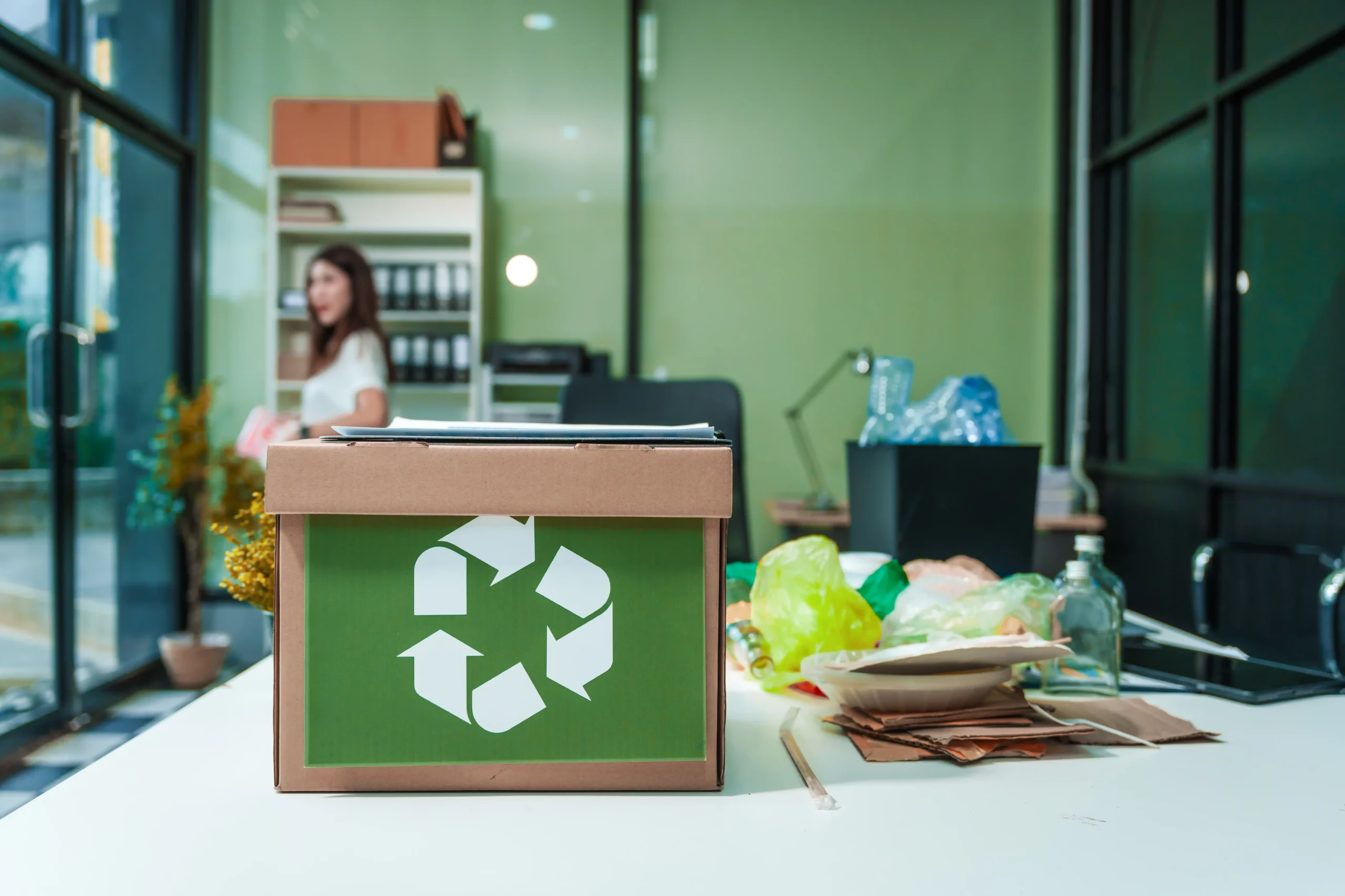 Eco-friendly desk setup with a recycling bin, reusable items, and plants promoting waste management.