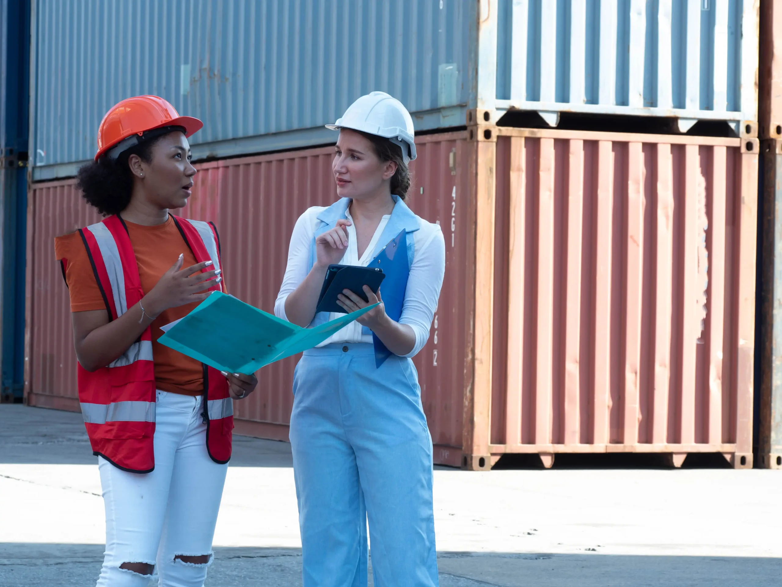 Two female logistics professionals discussing shipping documentation at a cargo terminal.