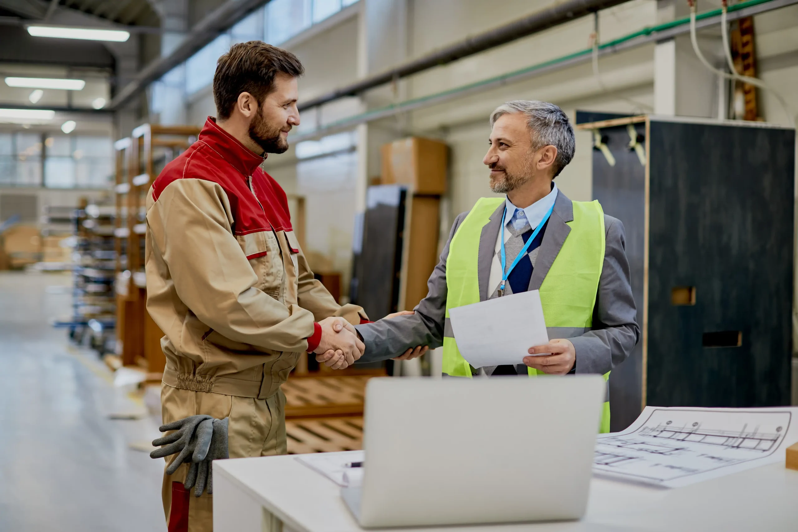 Woodworker and company manager shaking hands over tariff management and trade compliance agreement in a warehouse.