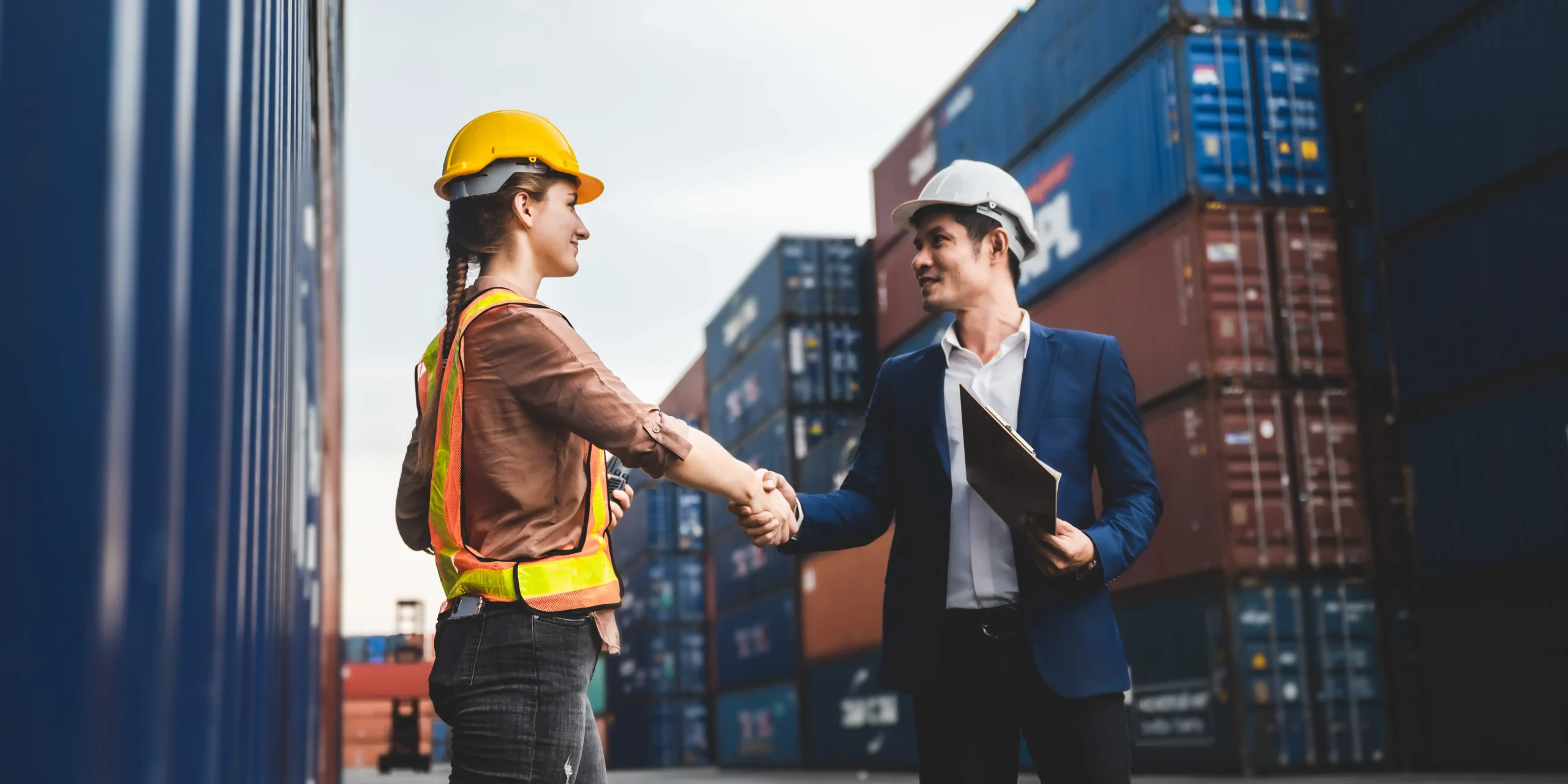 Logistics worker and foreman shaking hands amidst shipping containers.