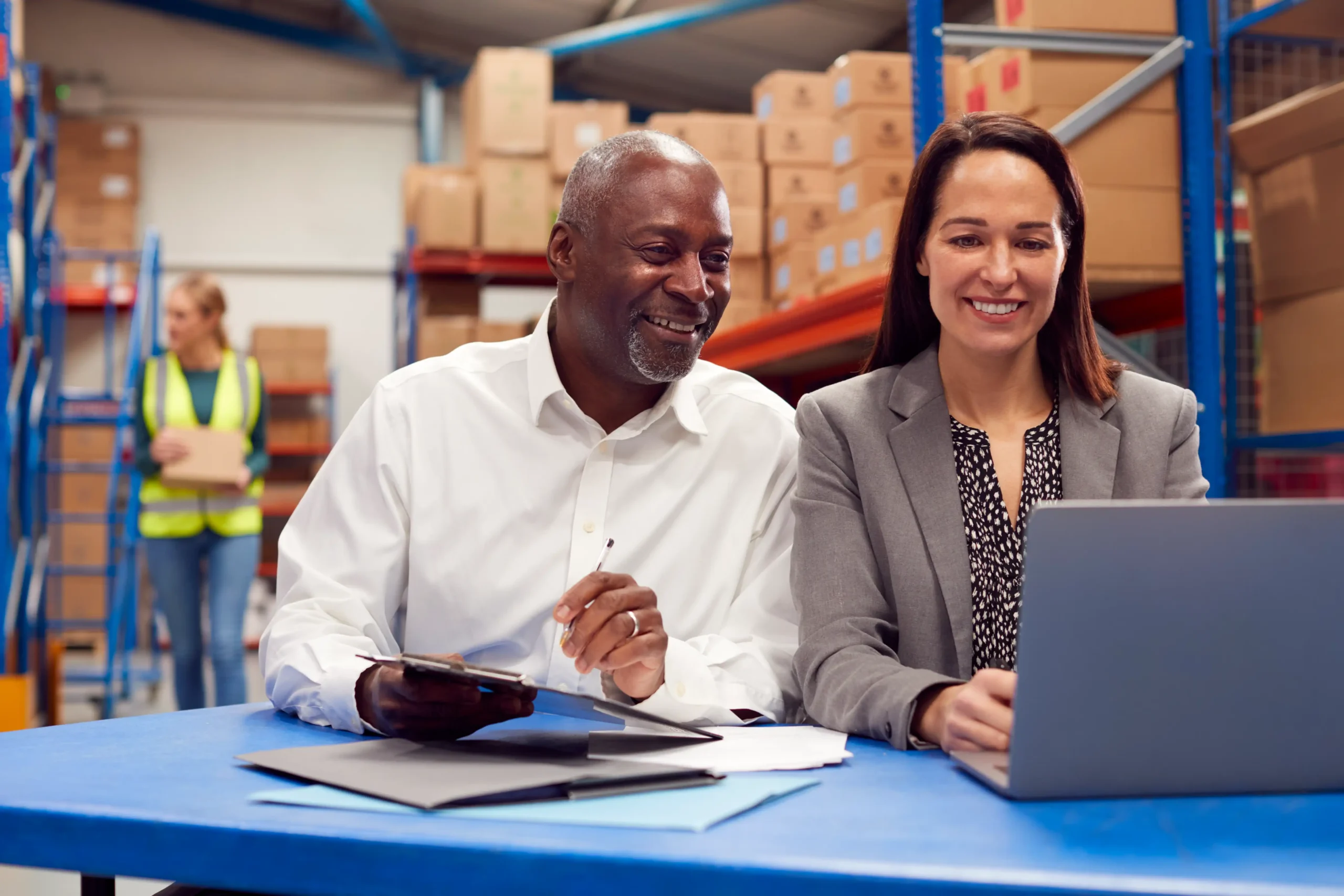 Male and female team leaders using a laptop to plan logistics in a warehouse office.