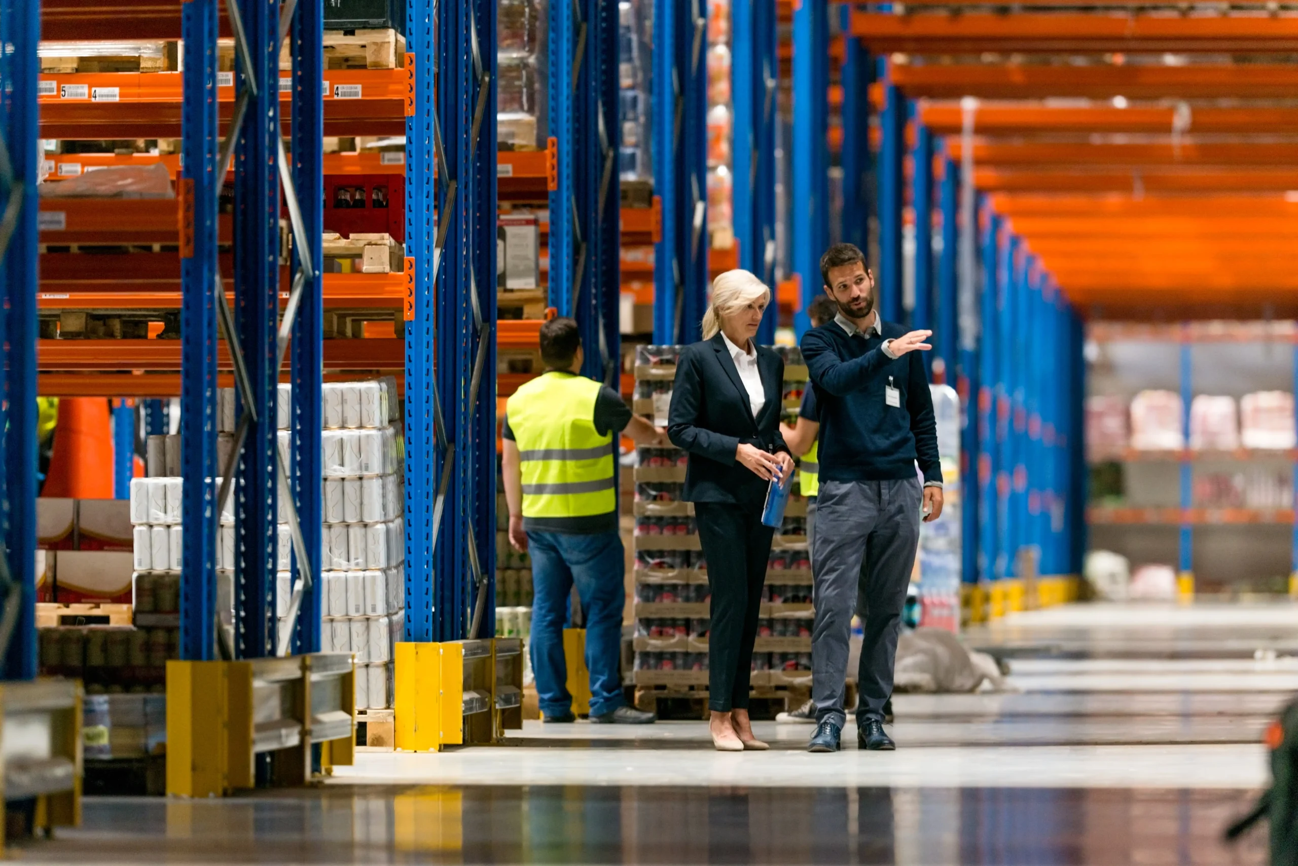 Warehouse manager discussing duty deferment strategies with team member in a large industrial storage facility.