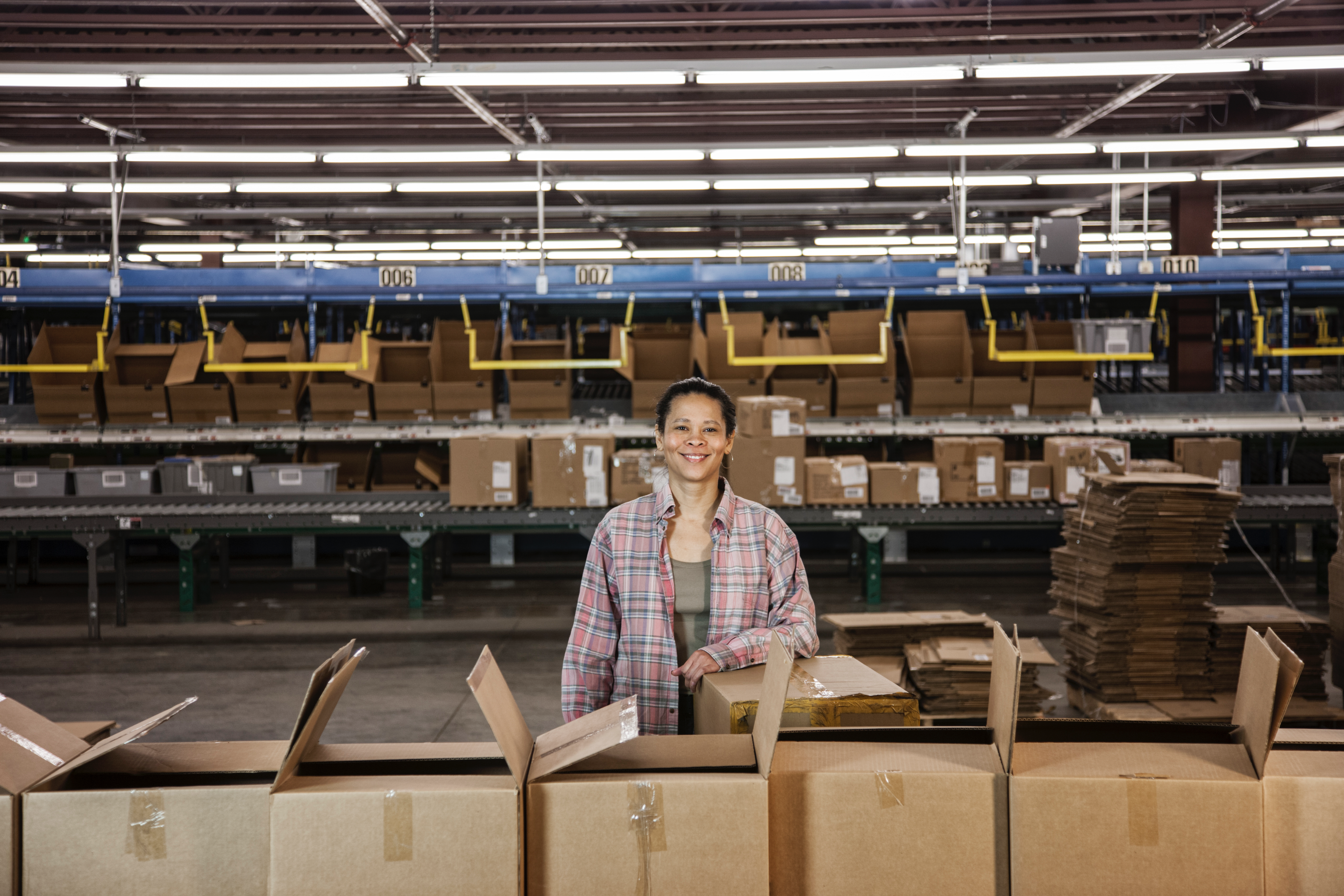 Smiling warehouse worker managing order fulfillment with boxes on conveyor belts in a modern facility.