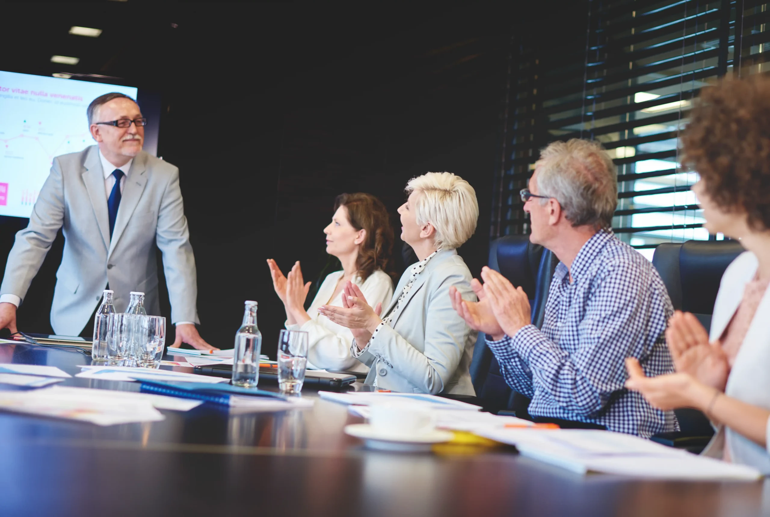 Senior business leaders applauding a presentation on compliance success.