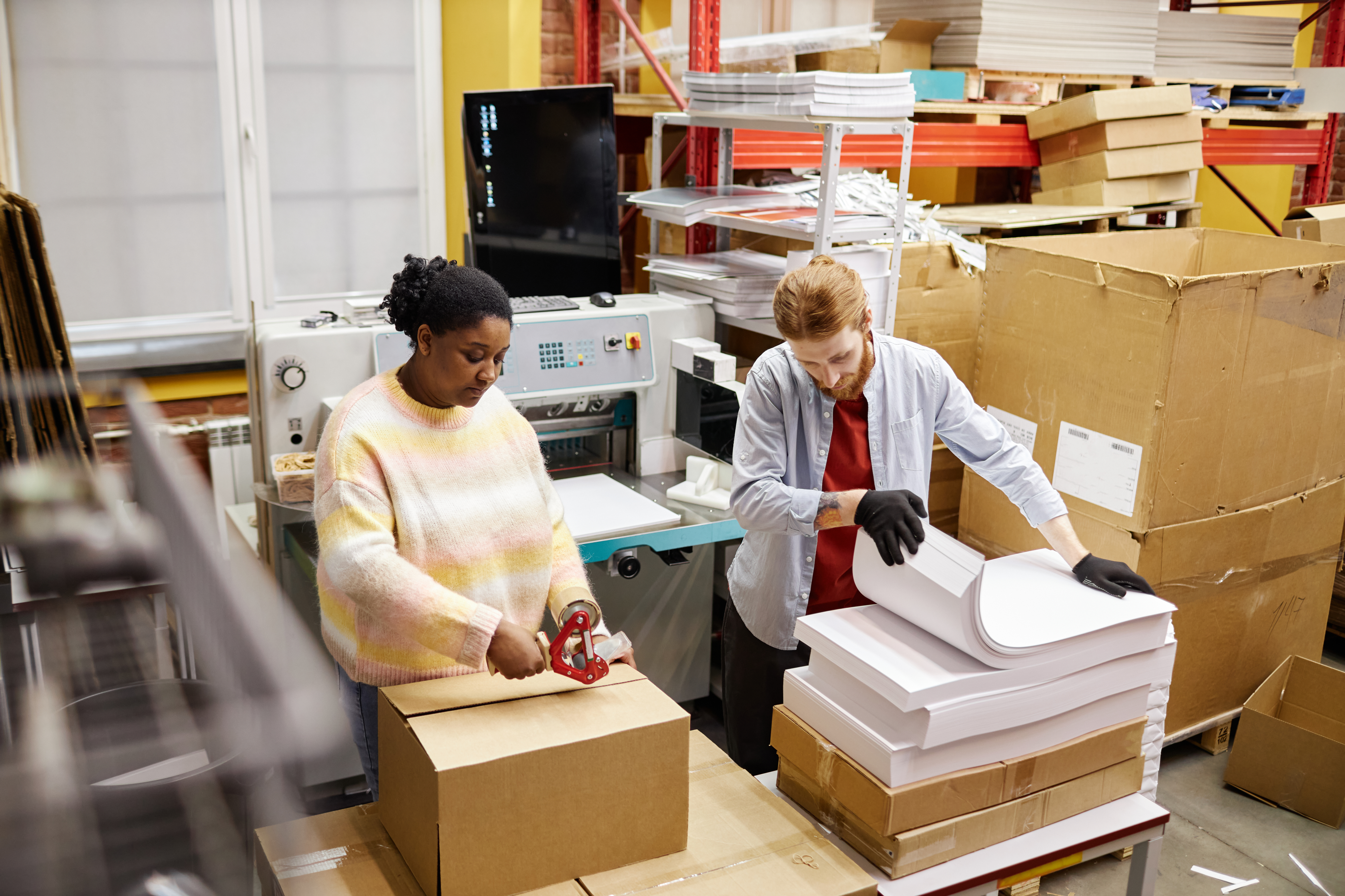 Workers preparing orders and packaging products in a busy printing and fulfillment factory.