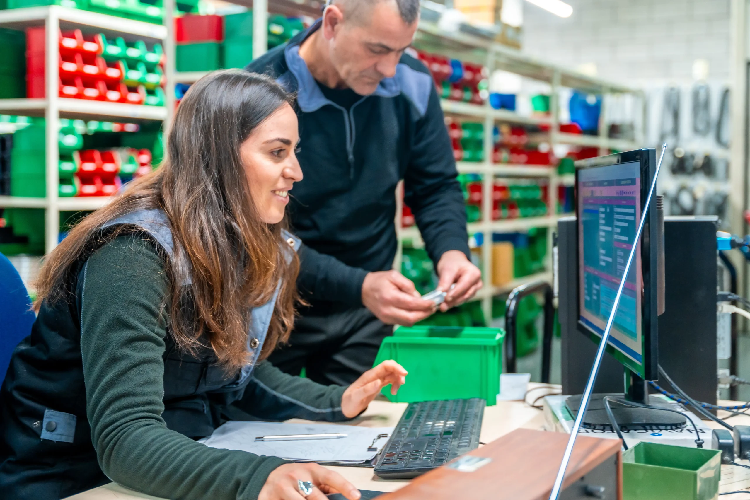 Workers using logistics software on a computer to manage inventory in a modern warehouse.