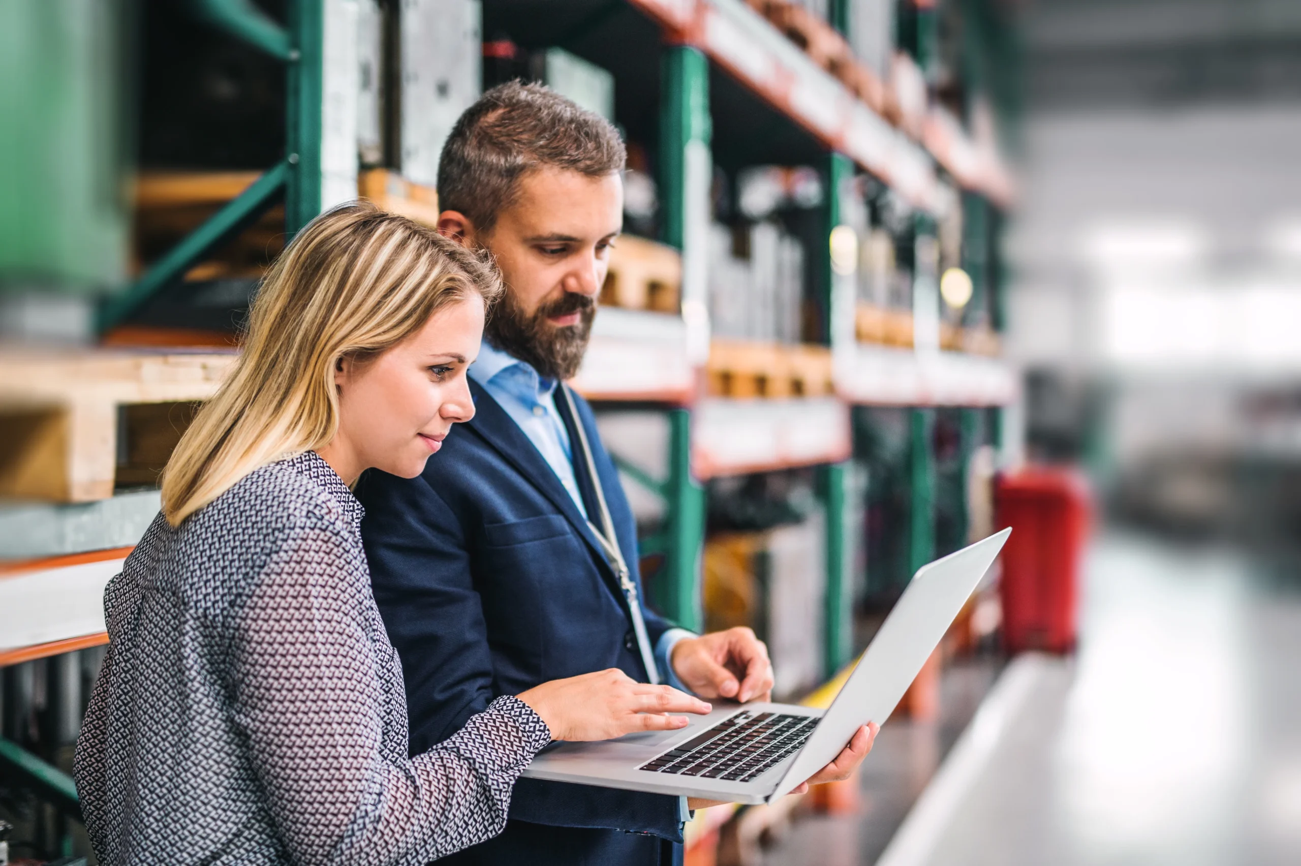 Industrial professionals analyzing data on a laptop in a warehouse setting, demonstrating supply chain optimization strategies.