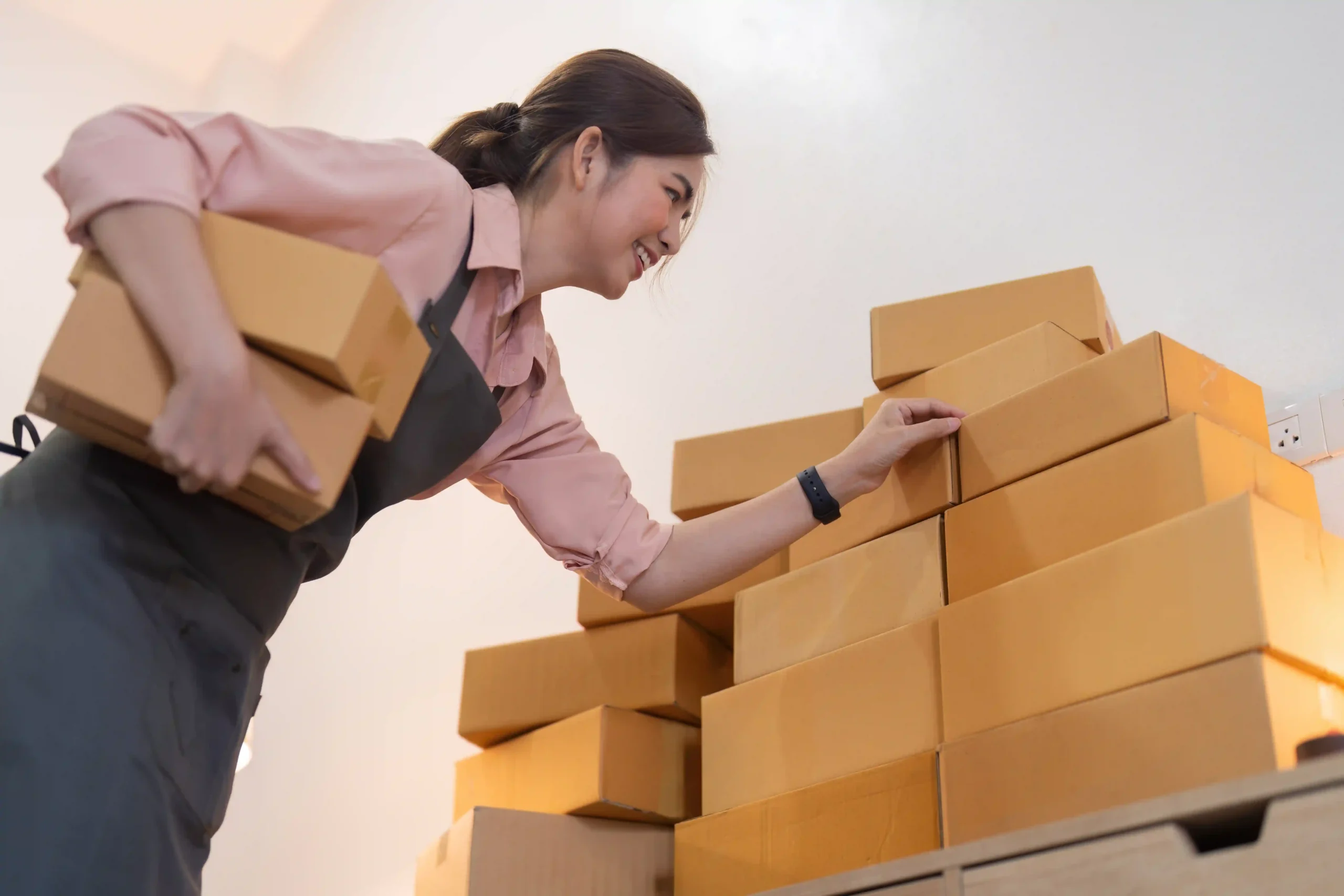 A smiling entrepreneur organizes parcel boxes on a shelf in preparation for shipping, demonstrating efficient fulfillment processes.