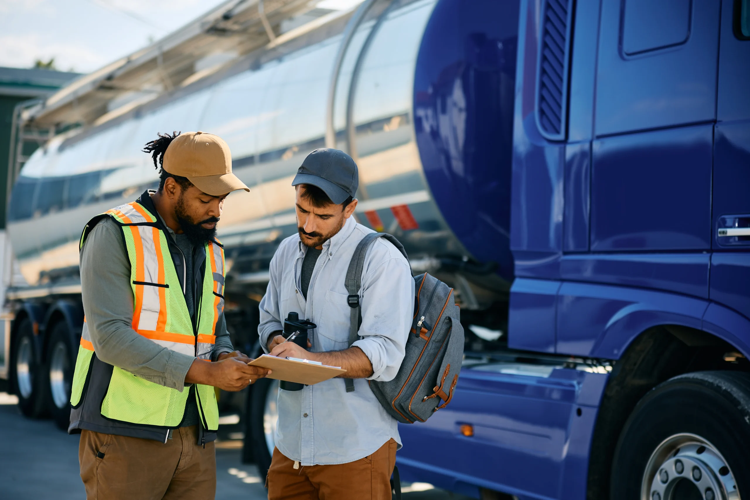 Logistics manager and truck driver reviewing shipment details in front of a delivery truck.