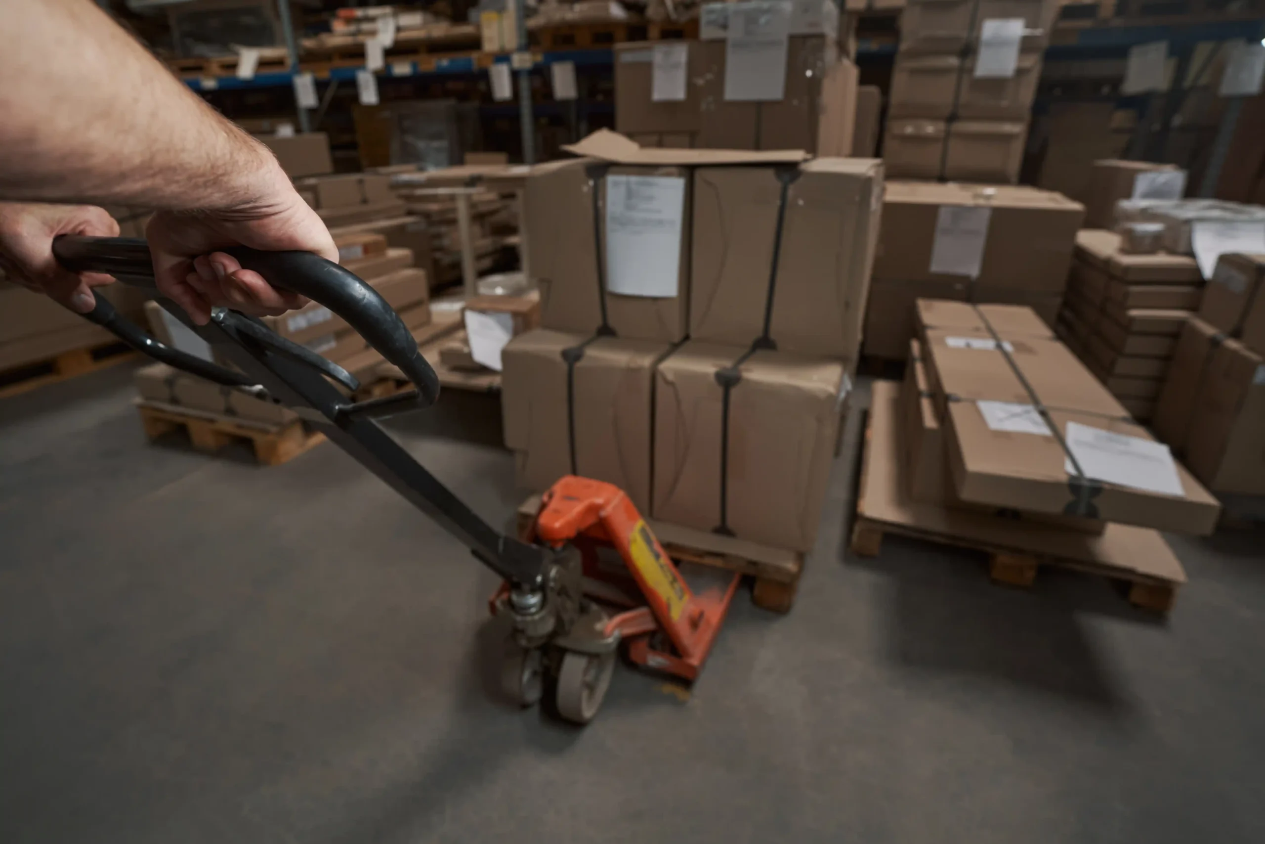 Close-up of a warehouse worker preparing boxes for delivery using a pallet jack.