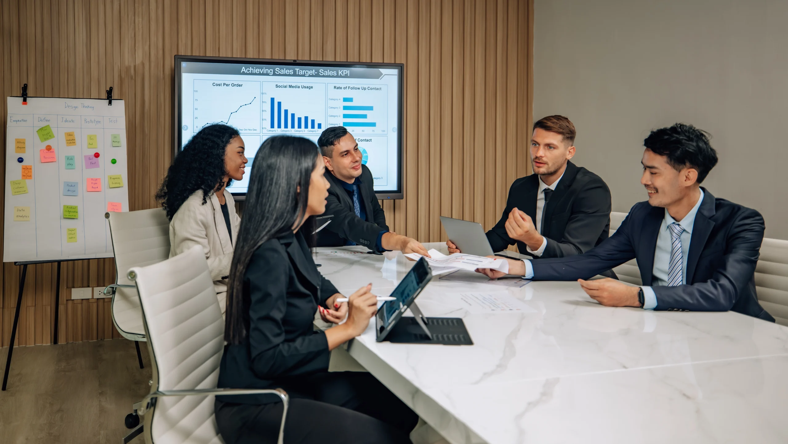 A diverse team discussing sales KPIs and data insights during a collaborative meeting, with graphs displayed on a screen.