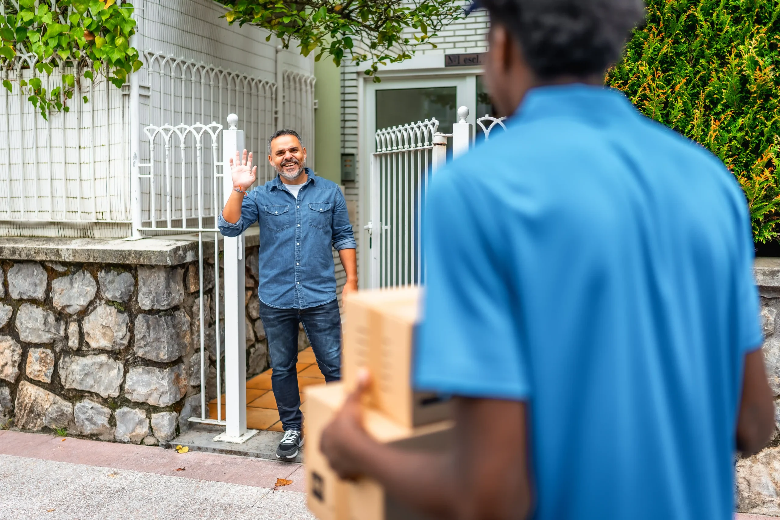 Man waving to a delivery driver carrying packages to his doorstep.