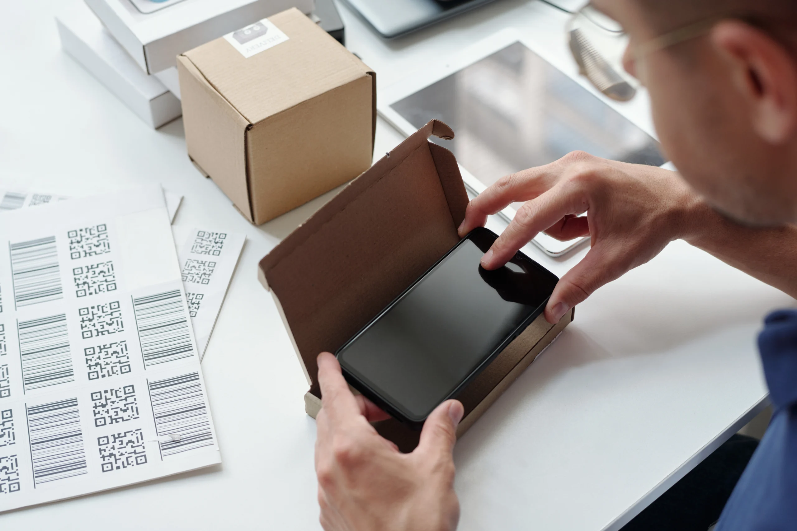 Packaging a smartphone in a box with printed barcode labels for product identification.