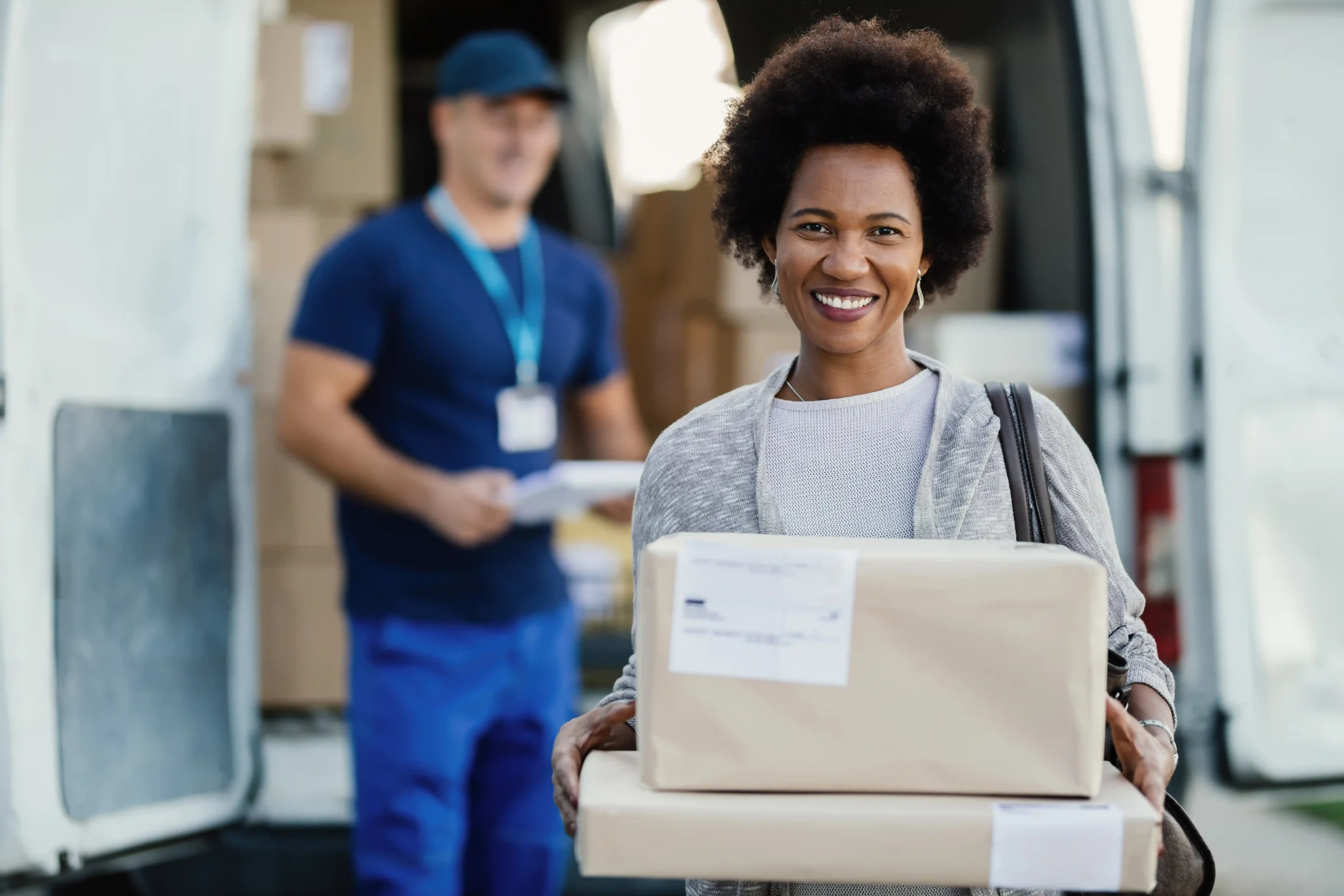 Happy woman holding her delivered package with a delivery driver in the background.