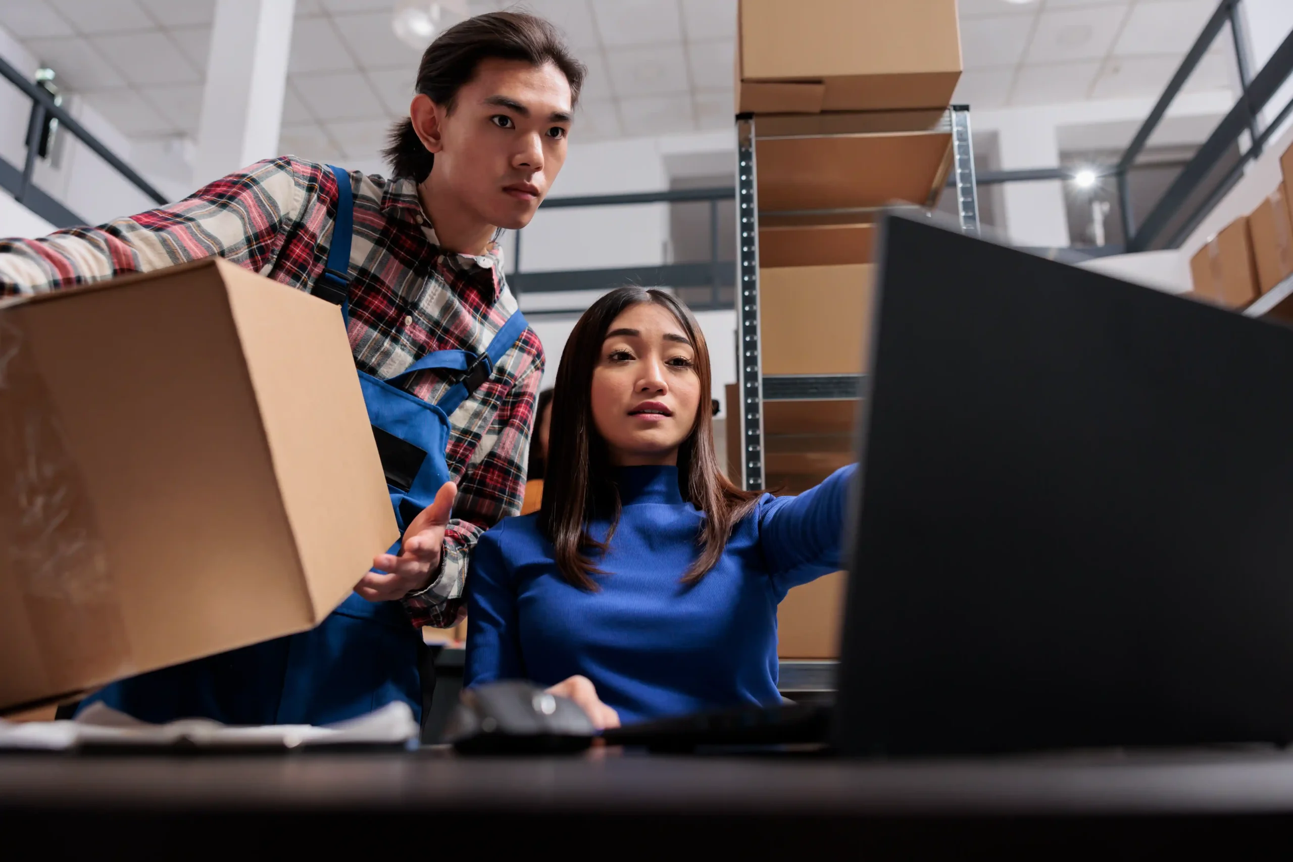 Asian warehouse workers preparing packages and managing inventory using a computer.