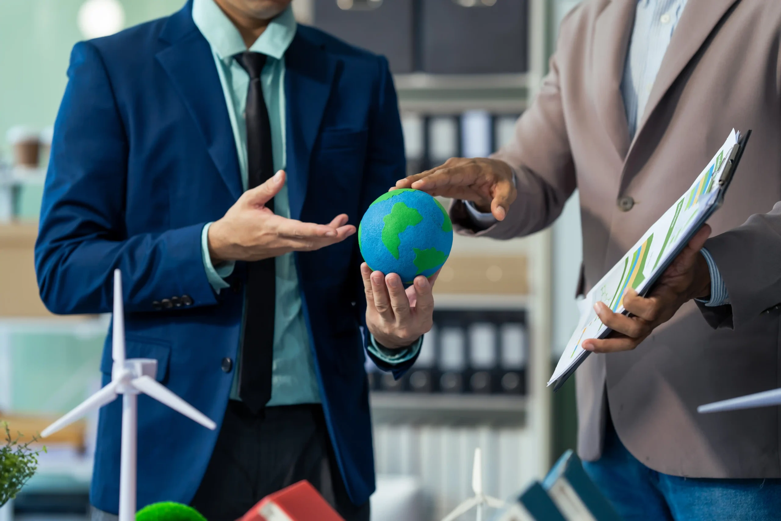 Two businessmen in formal suits discussing sustainable business strategies with a focus on a globe and eco-friendly models.