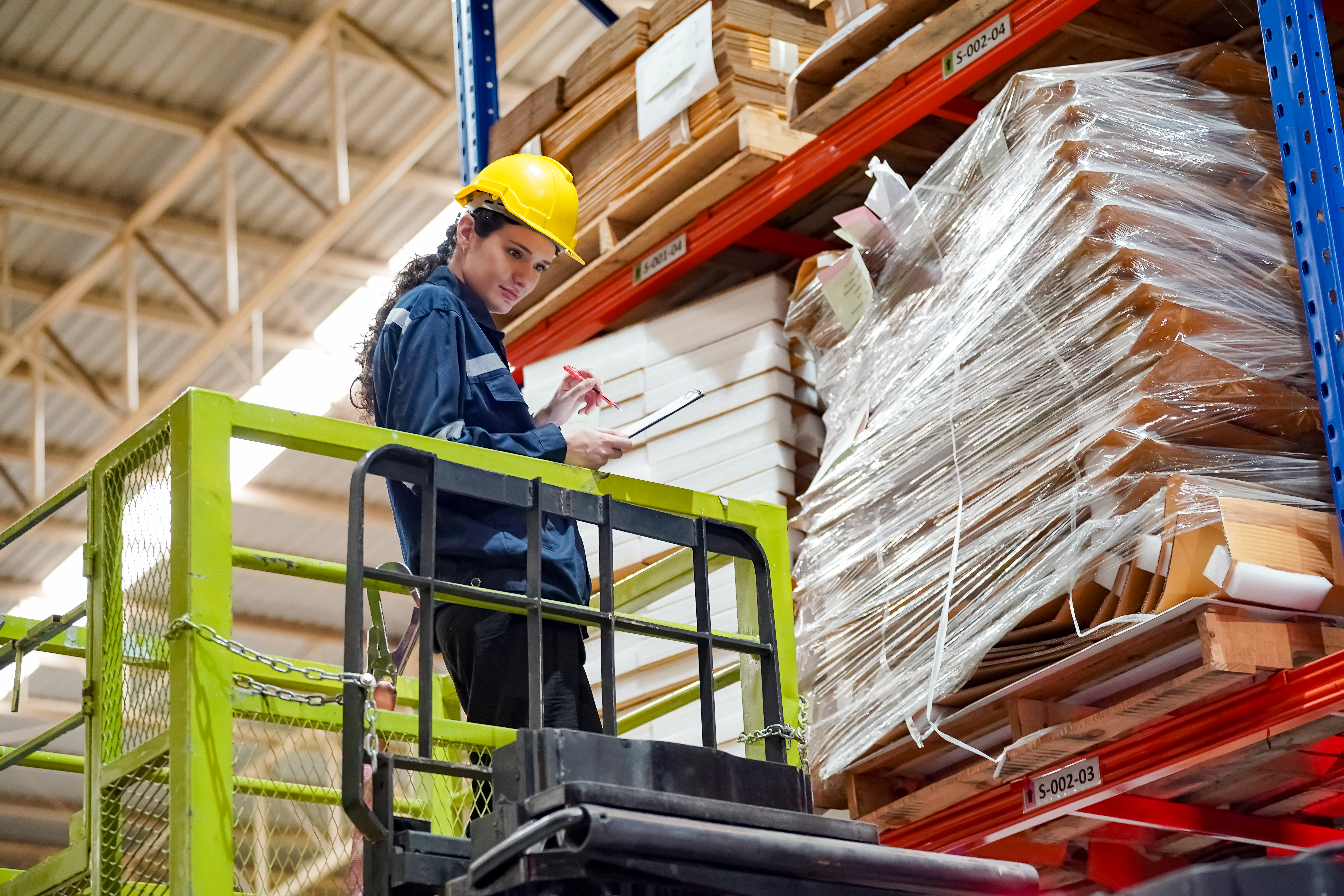 Female warehouse worker inspecting shrink-wrapped palletized goods in a distribution center.