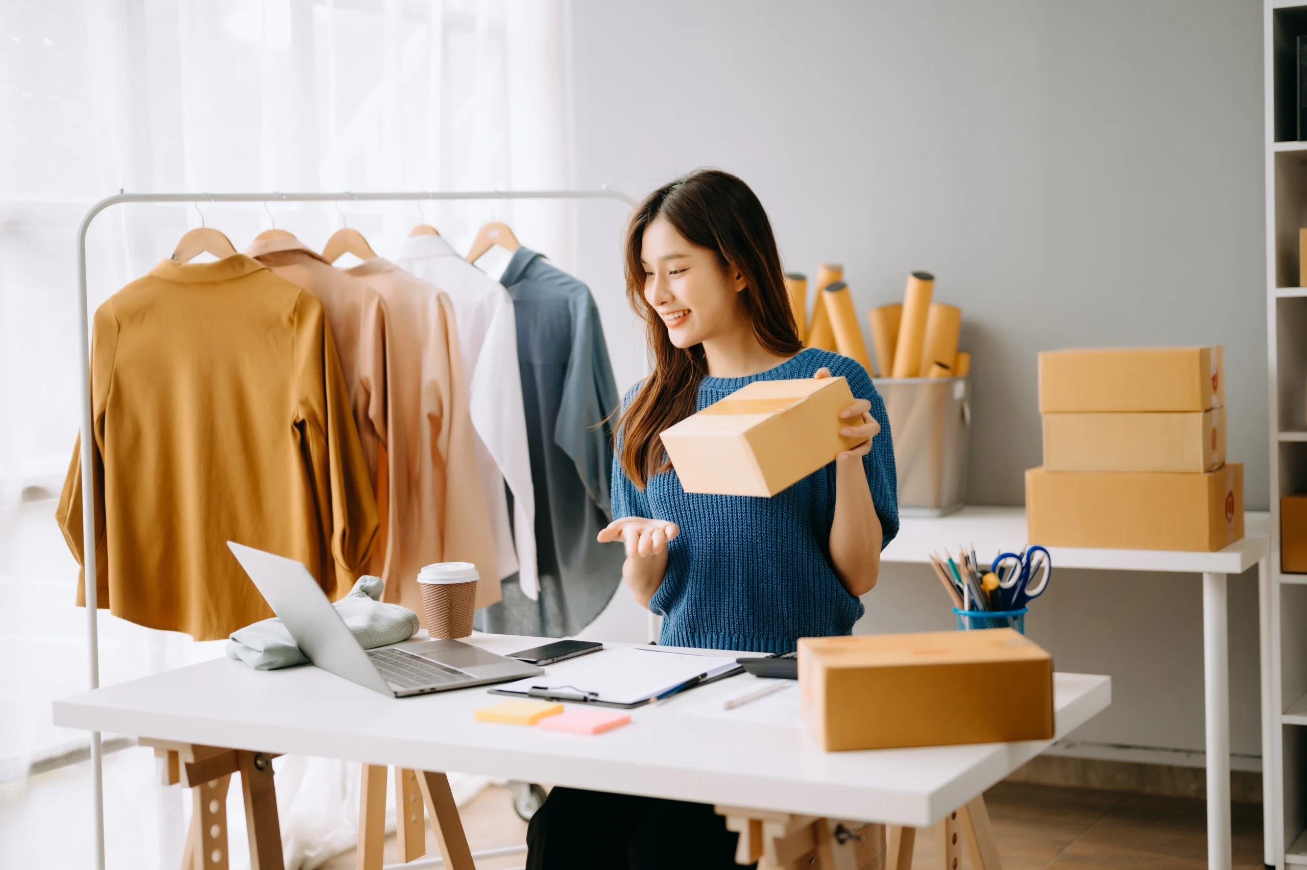 Woman handling packaging for e-commerce orders with a laptop and delivery boxes at her workspace, showcasing 3PL value-added services for kitting and order fulfillment.