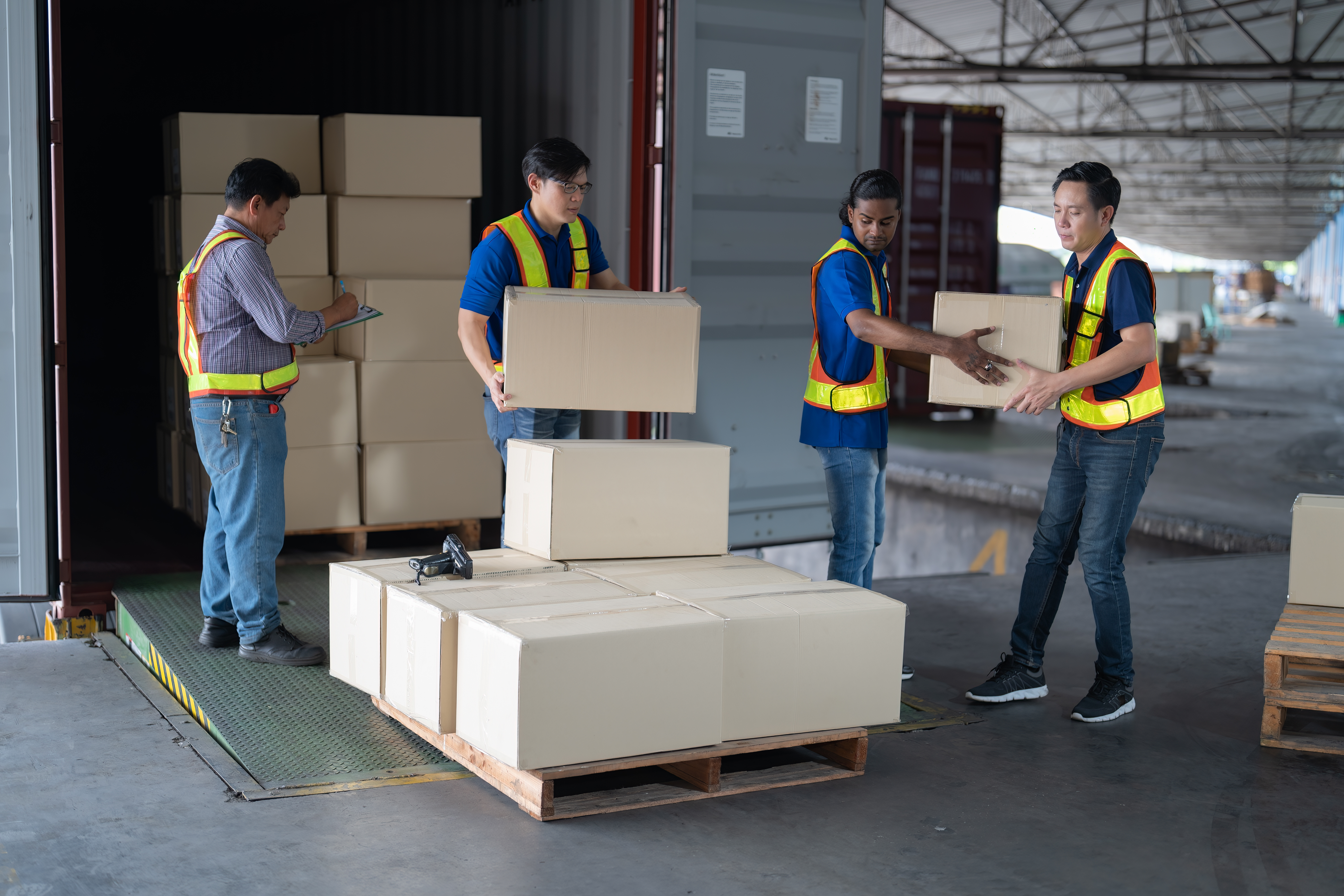 Workers organizing and loading palletized boxes into a steel shipping container for transport.