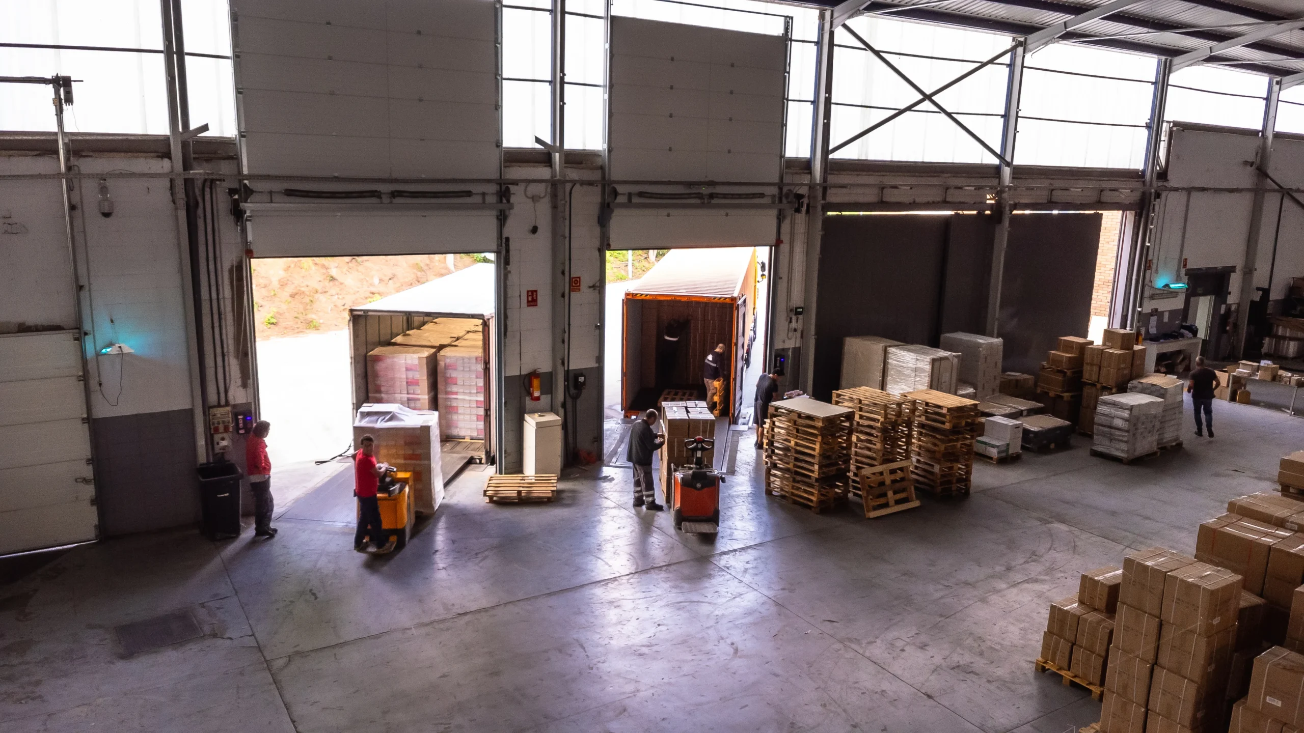 Aerial view of a cross-docking area in a distribution warehouse with workers loading pallets into trailers for outbound shipments.