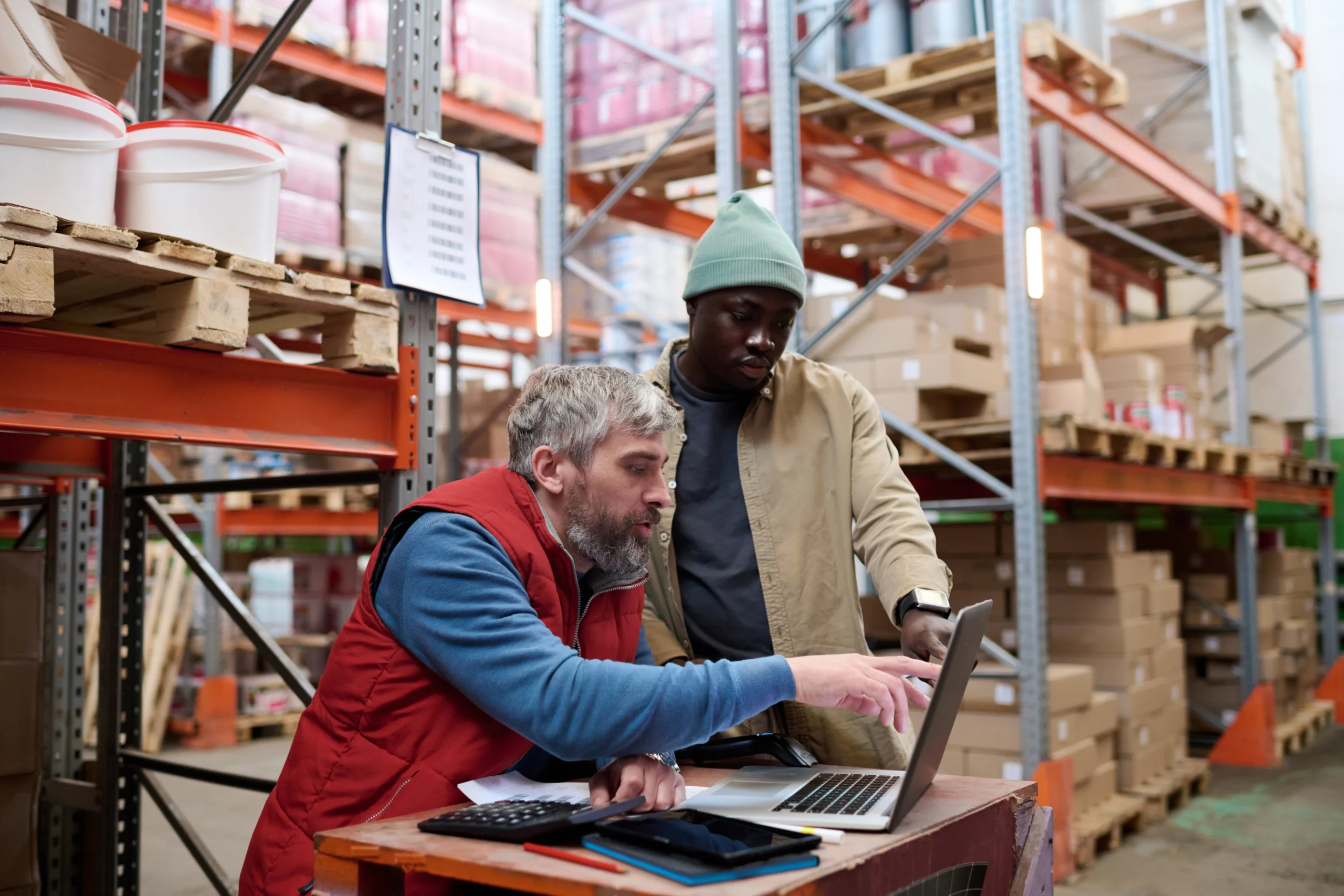 Warehouse employees managing inventory using a laptop, ensuring accurate stock tracking and efficient inventory management support.