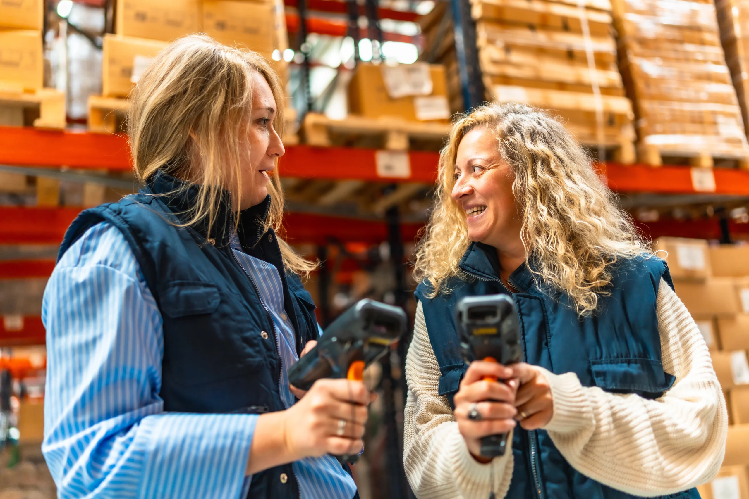 Two warehouse workers using barcode scanners to track inventory in a distribution center, optimizing workflow with linear barcode types.