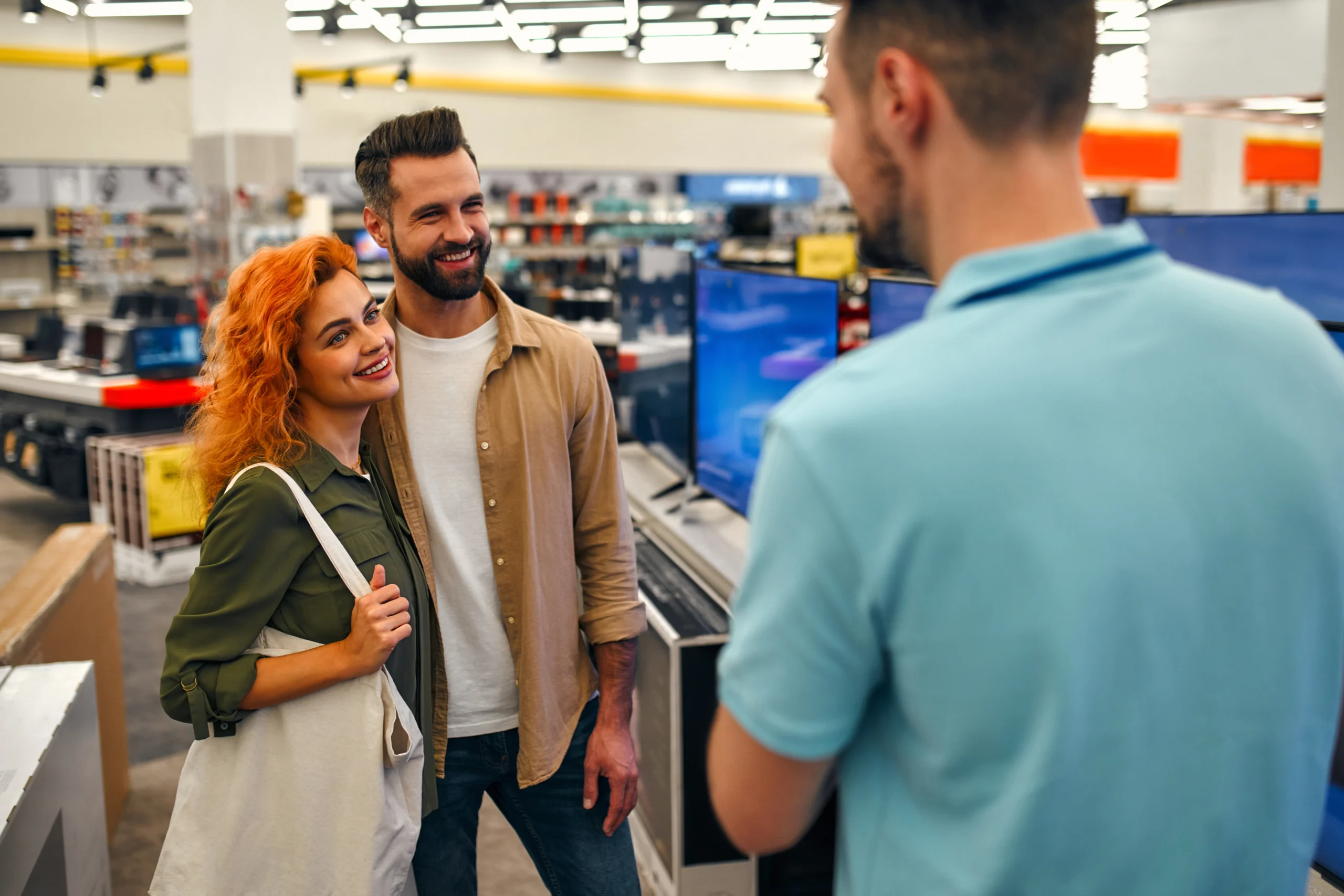 A couple speaking with a store associate in an electronics store, receiving in-person customer service similar to Pick and Save’s support experience.