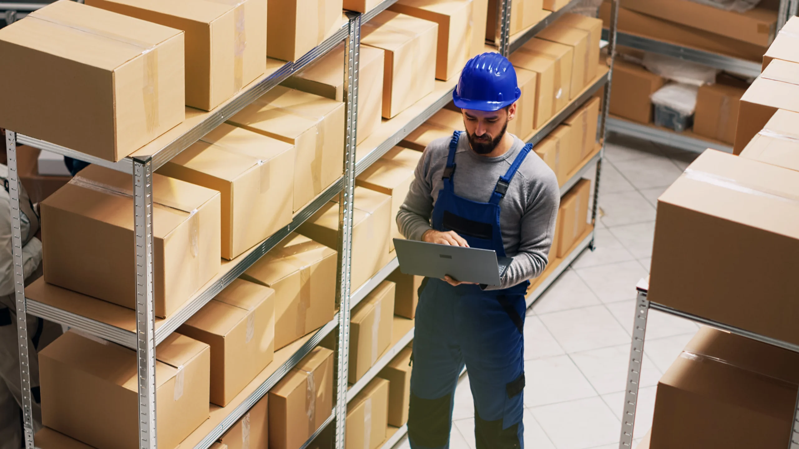 Warehouse supervisor using a laptop to update stock levels with an inventory management system in Google Sheets.