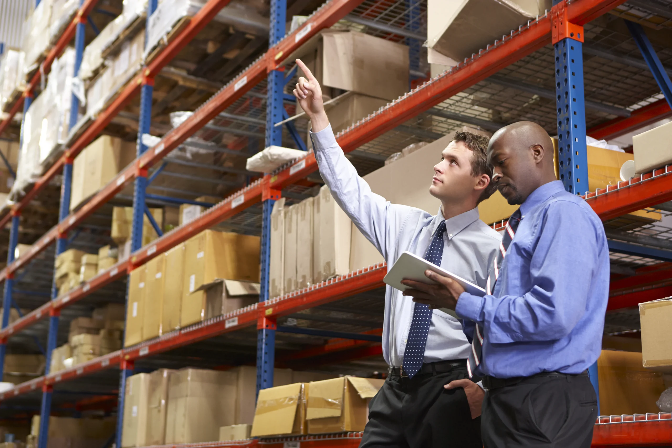 Two inventory managers using a digital tablet to analyze stock levels and optimize warehouse operations.