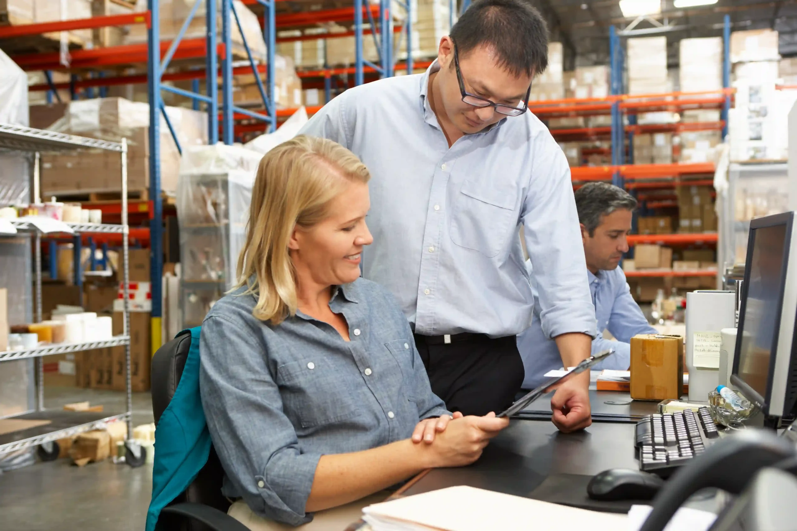 A Supply Chain Optimization Analyst collaborating with a logistics manager in a warehouse office, discussing supply chain improvements and cost reduction strategies.