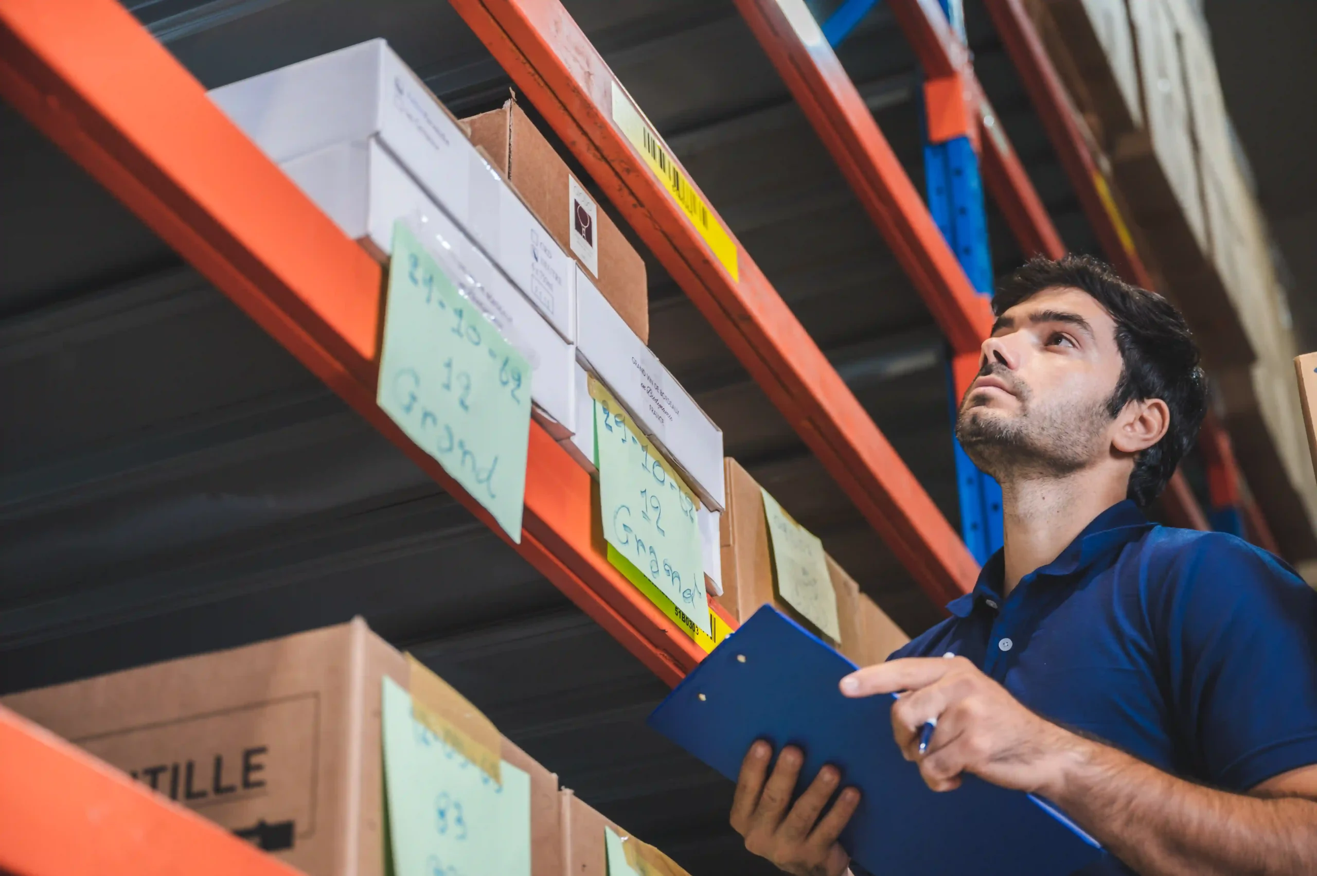 A logistics manager analyzing inventory stock levels in a warehouse with labeled shelves.