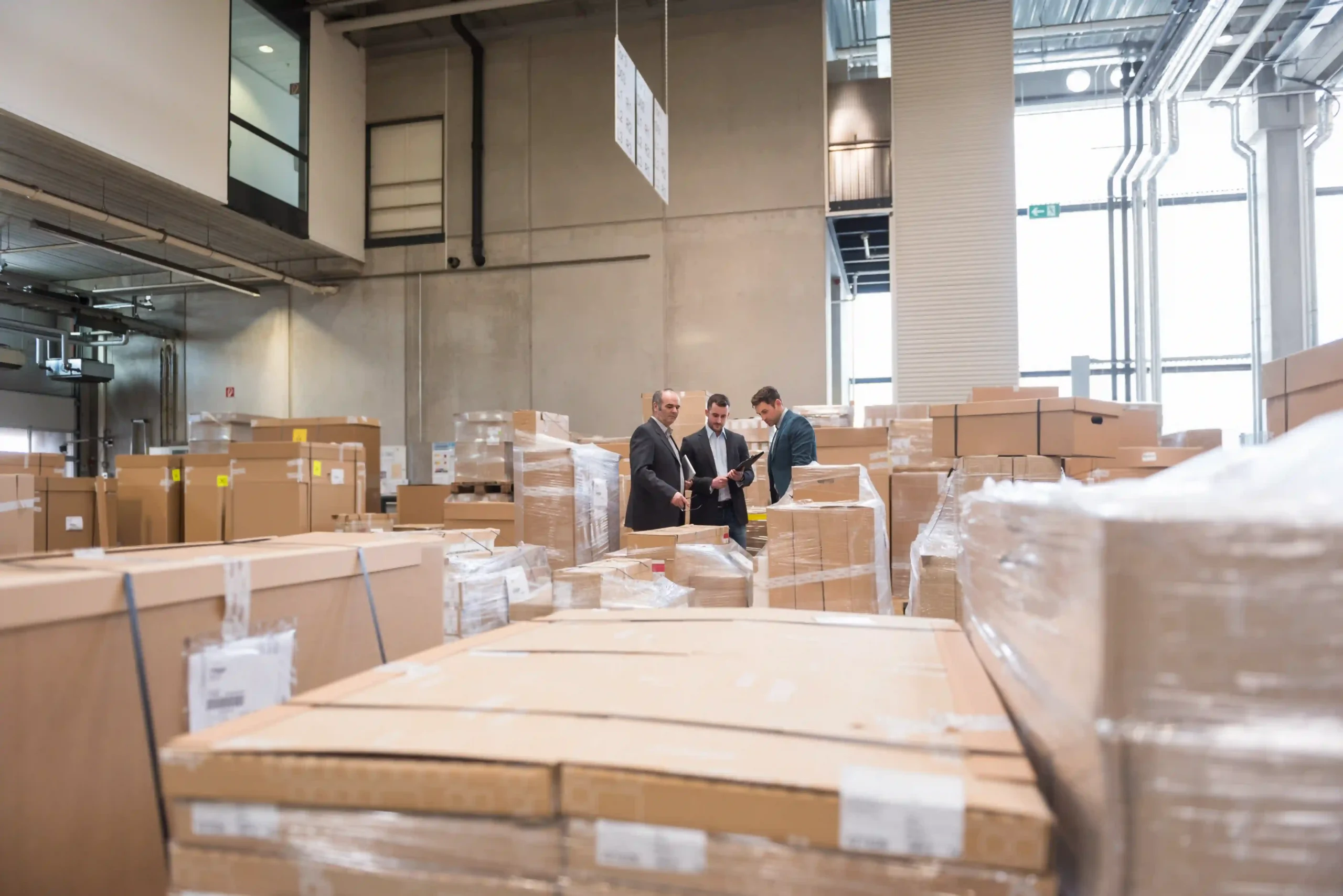 Three business professionals strategizing FTZ warehouse operations among stacked inventory.