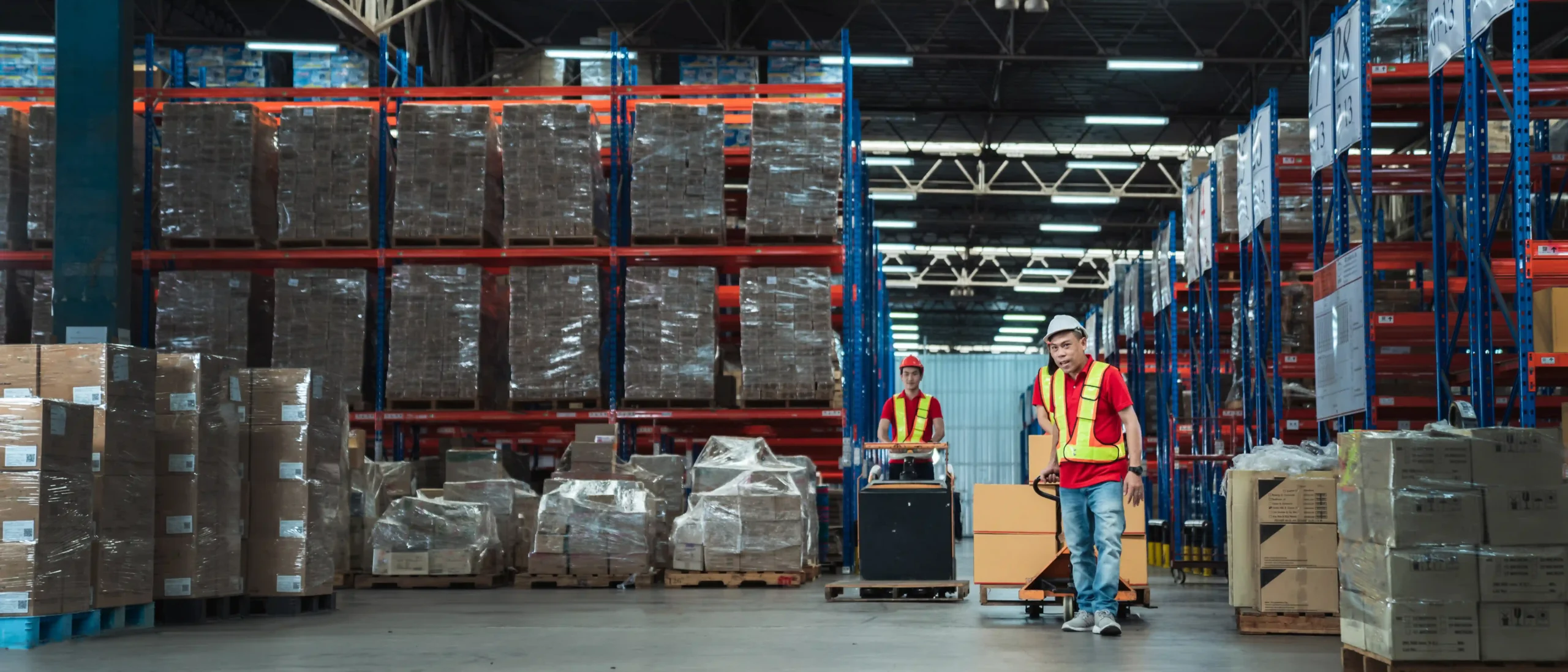 Warehouse workers inspecting stock in a well-organized warehouse bay with shelving, forklifts, and clear aisles.