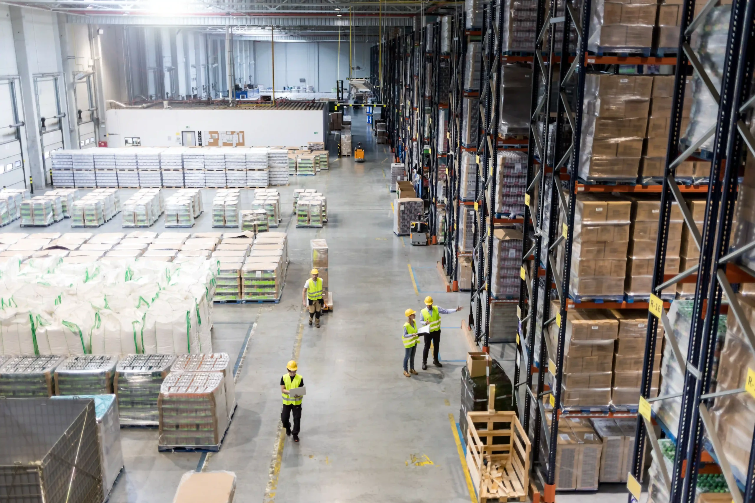 A large warehouse bay with tall industrial racks filled with pallets and workers managing inventory and logistics.