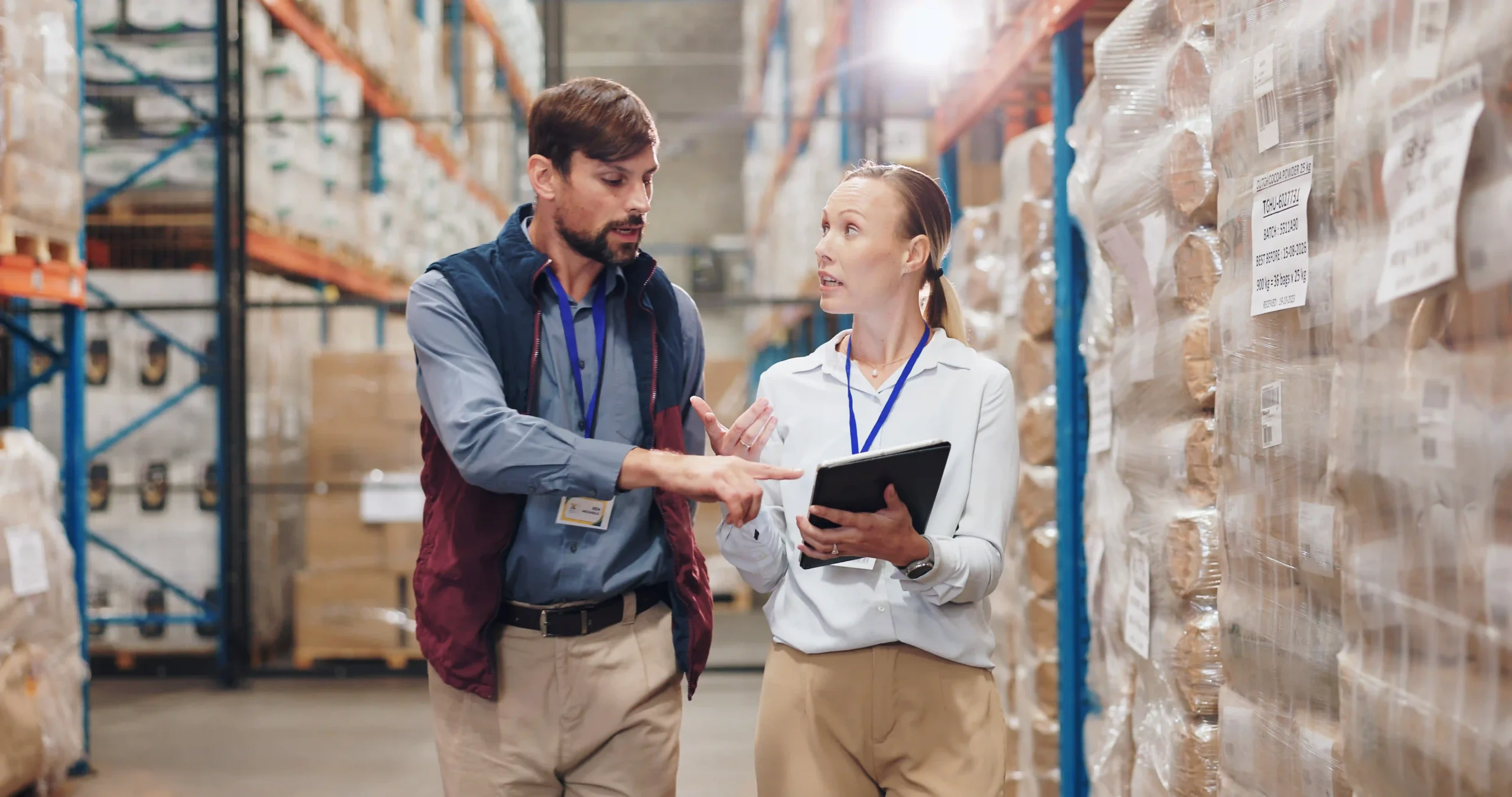 A supply chain optimization manager reviewing inventory levels on a tablet with a logistics team in a distribution center.