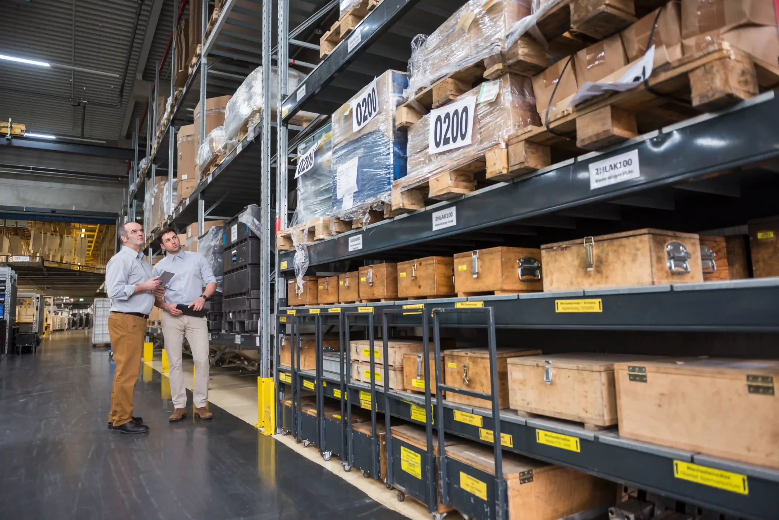 Logistics managers analyzing shelf layout and product flow inside a factory warehouse, representing warehousing logistics meaning